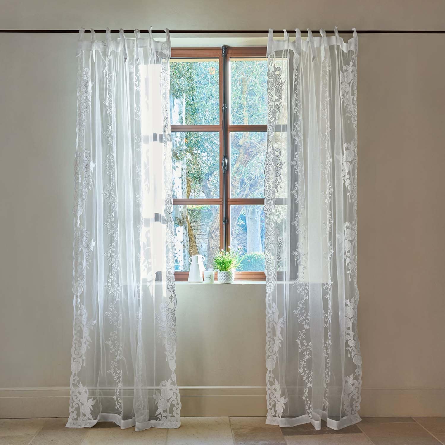 Cortinas blancas transparentes con bordado floral en ventana de madera clara
