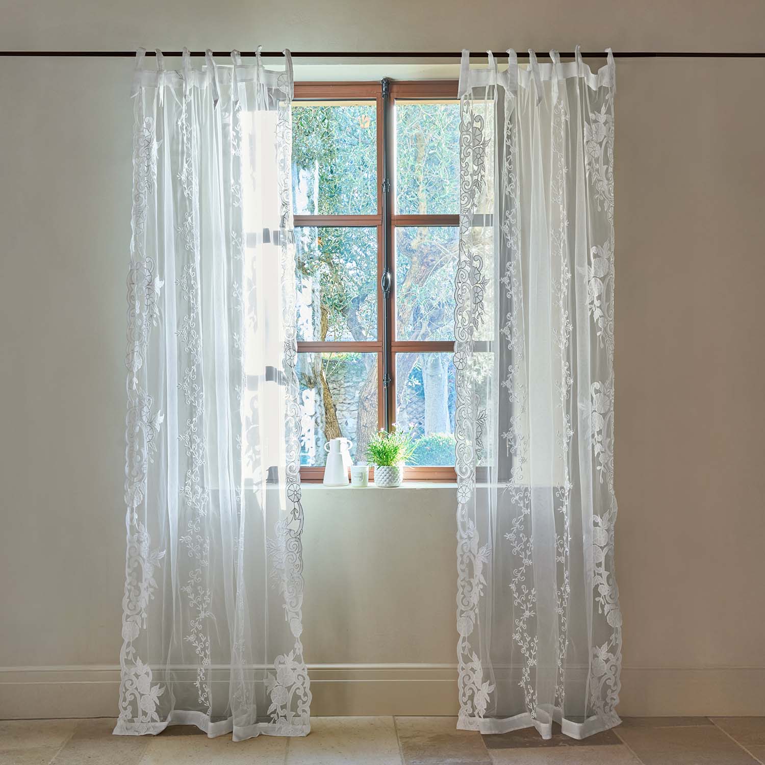 Cortinas blancas transparentes con bordado floral en ventana de madera clara