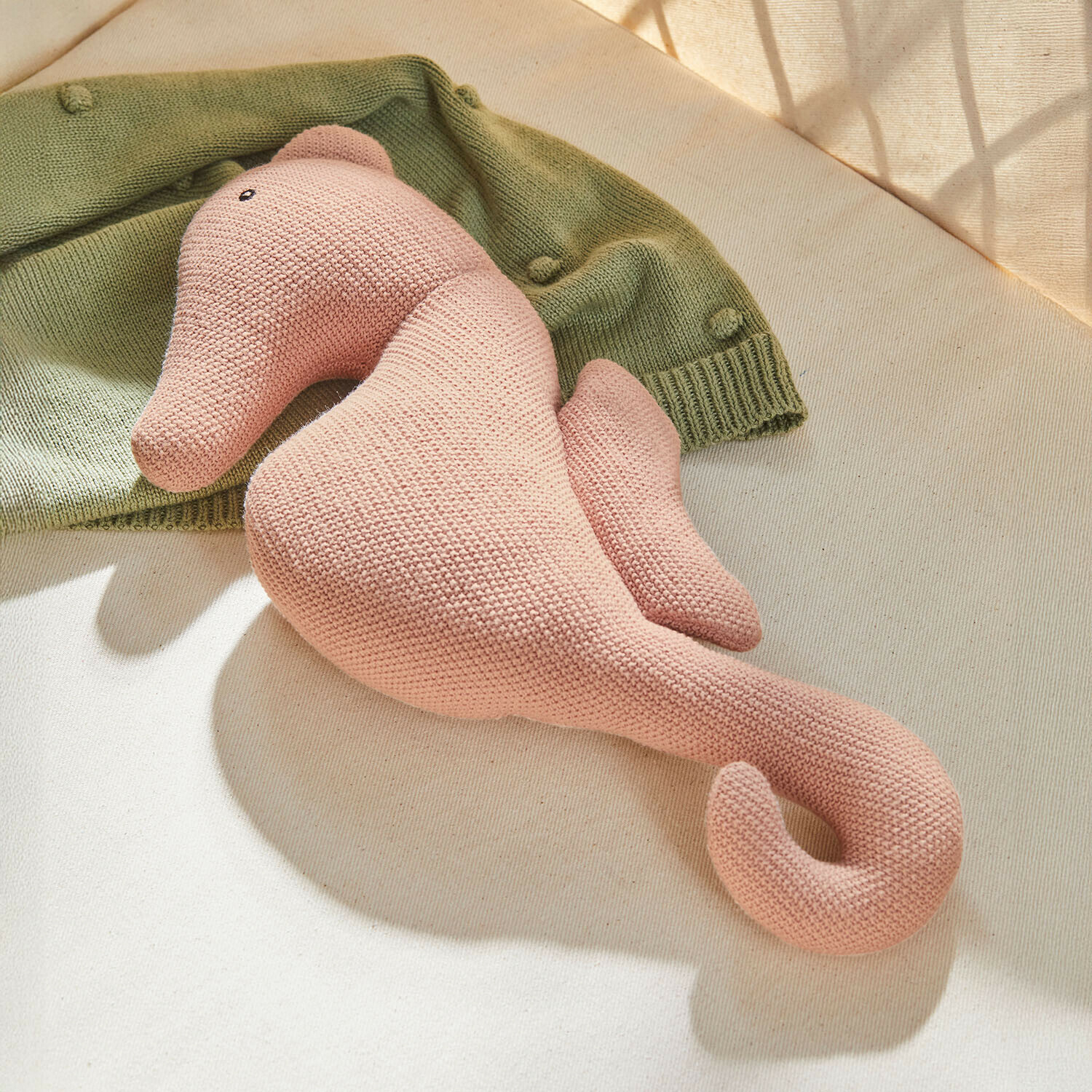 Caballito de mar de peluche rosa tejido sobre fondo claro con suéter verde, juguete suave para niños