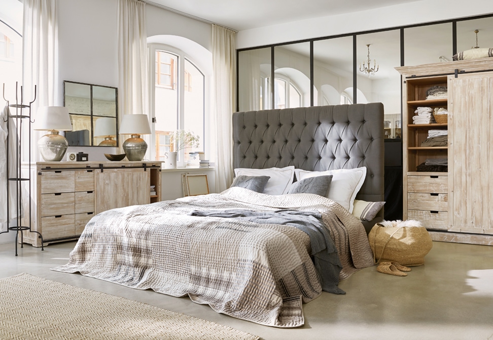 Dormitorio acogedor con cabecero gris acolchado y muebles de madera clara estilo loft