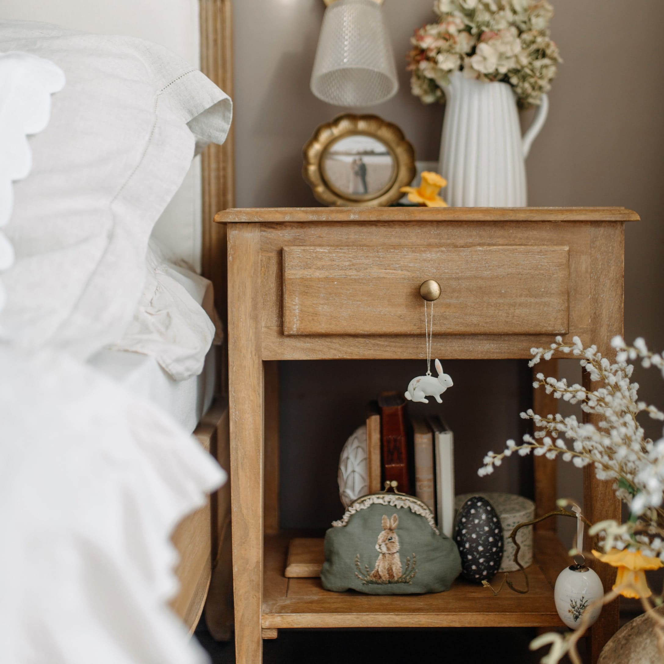 Mesita de noche de madera con decoraciones de Pascua y neceser verde con diseño de conejo en dormitorio