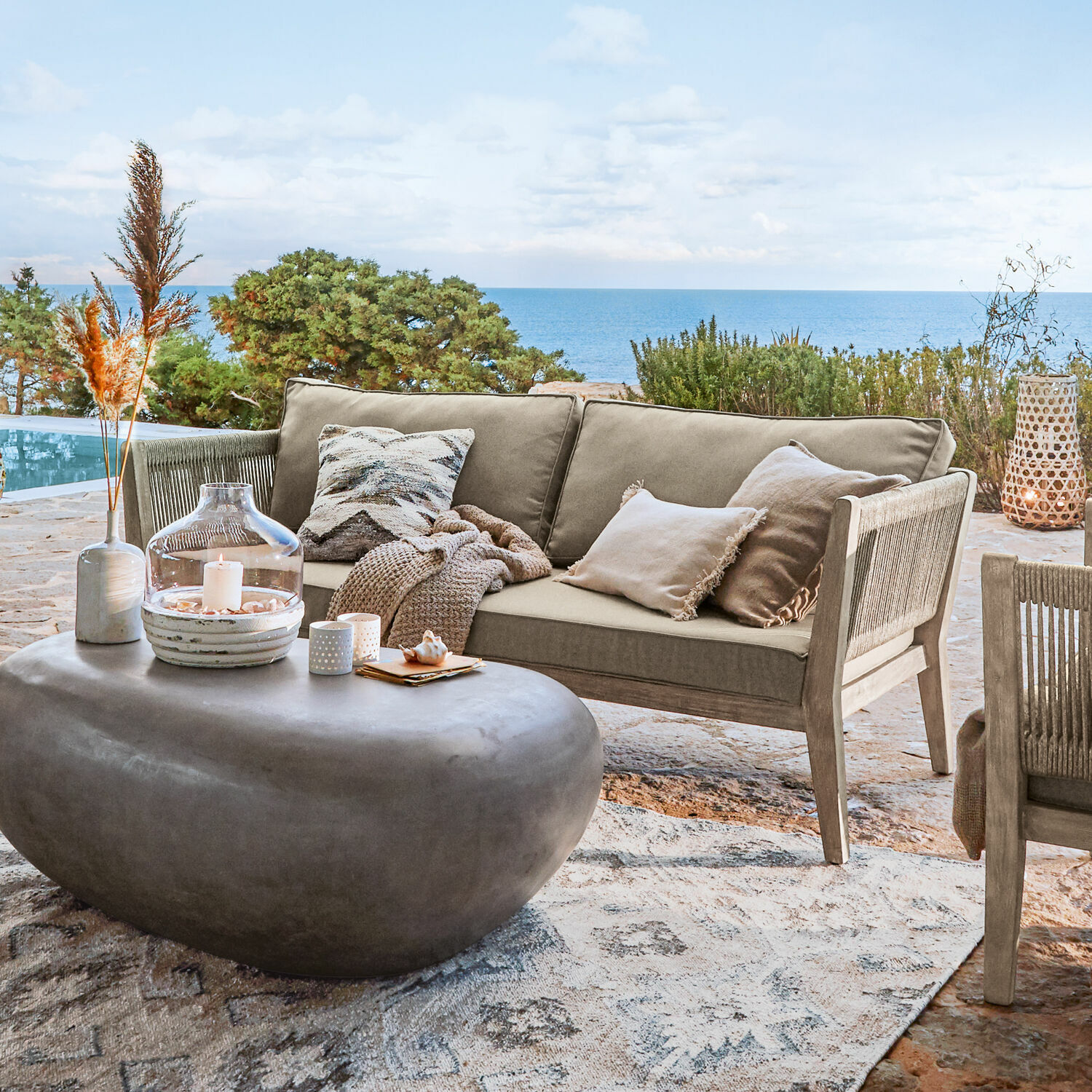Sofá de exterior beige de madera y tela en terraza con vista al mar, mesa de centro moderna