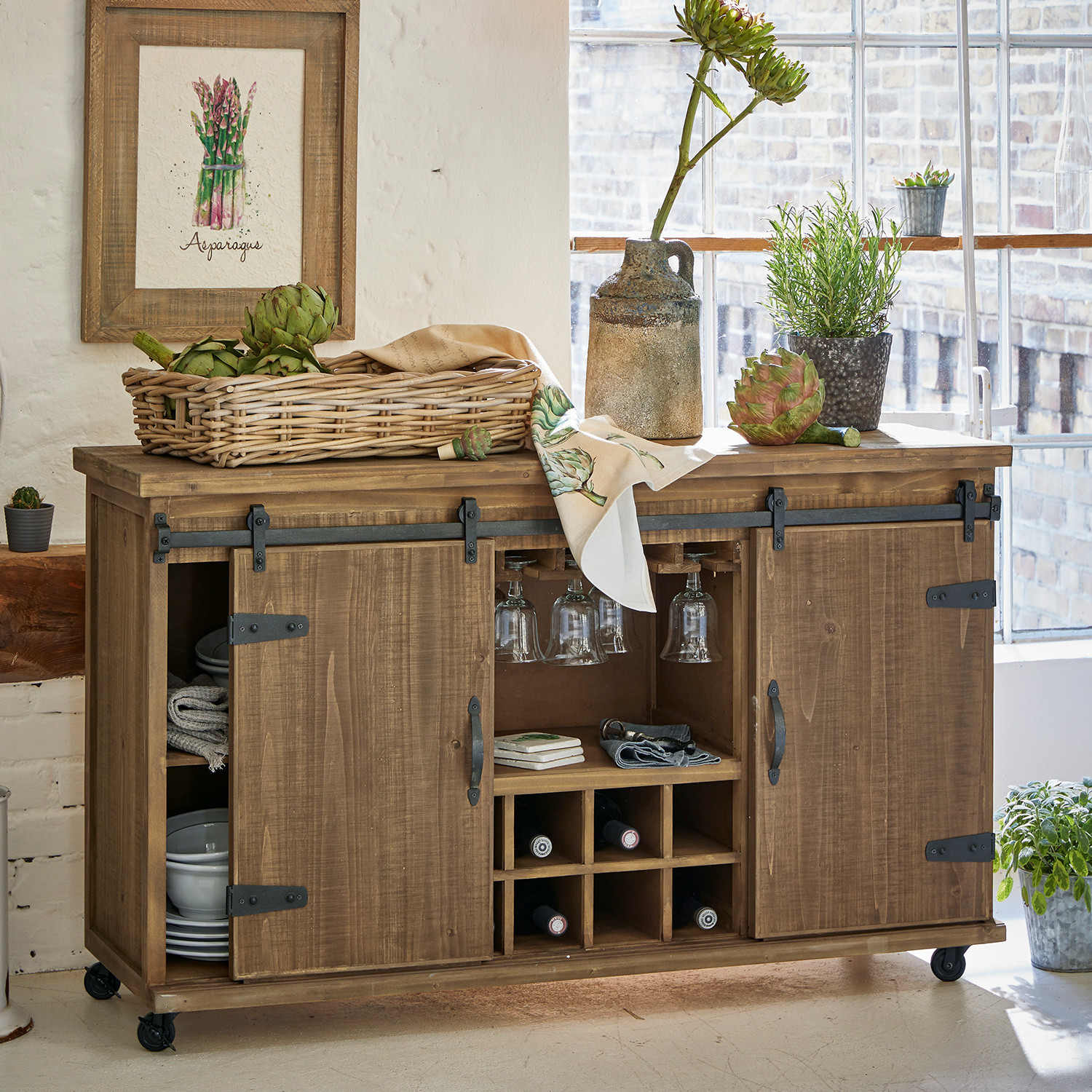 Cómoda Grasse Aparador de madera con ruedas con espacio para vino y copas, decorado con plantas verdes y cesta de verduras