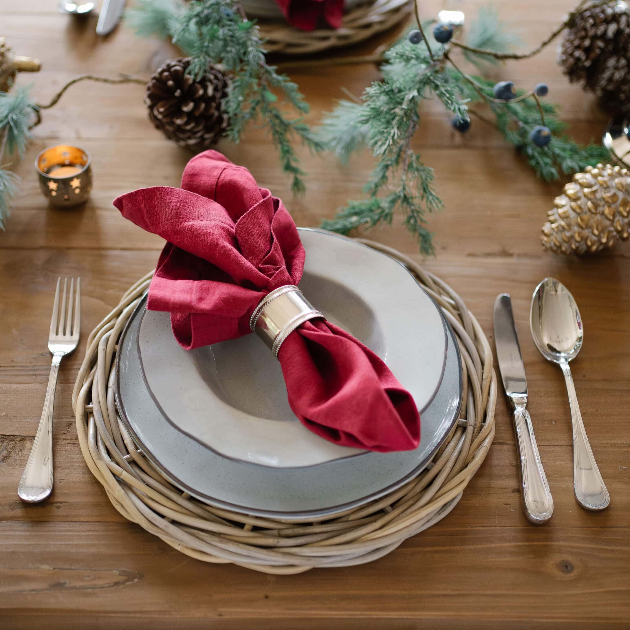 Servicio de mesa elegante con platos grises, servilleta roja de lino y base de mimbre natural