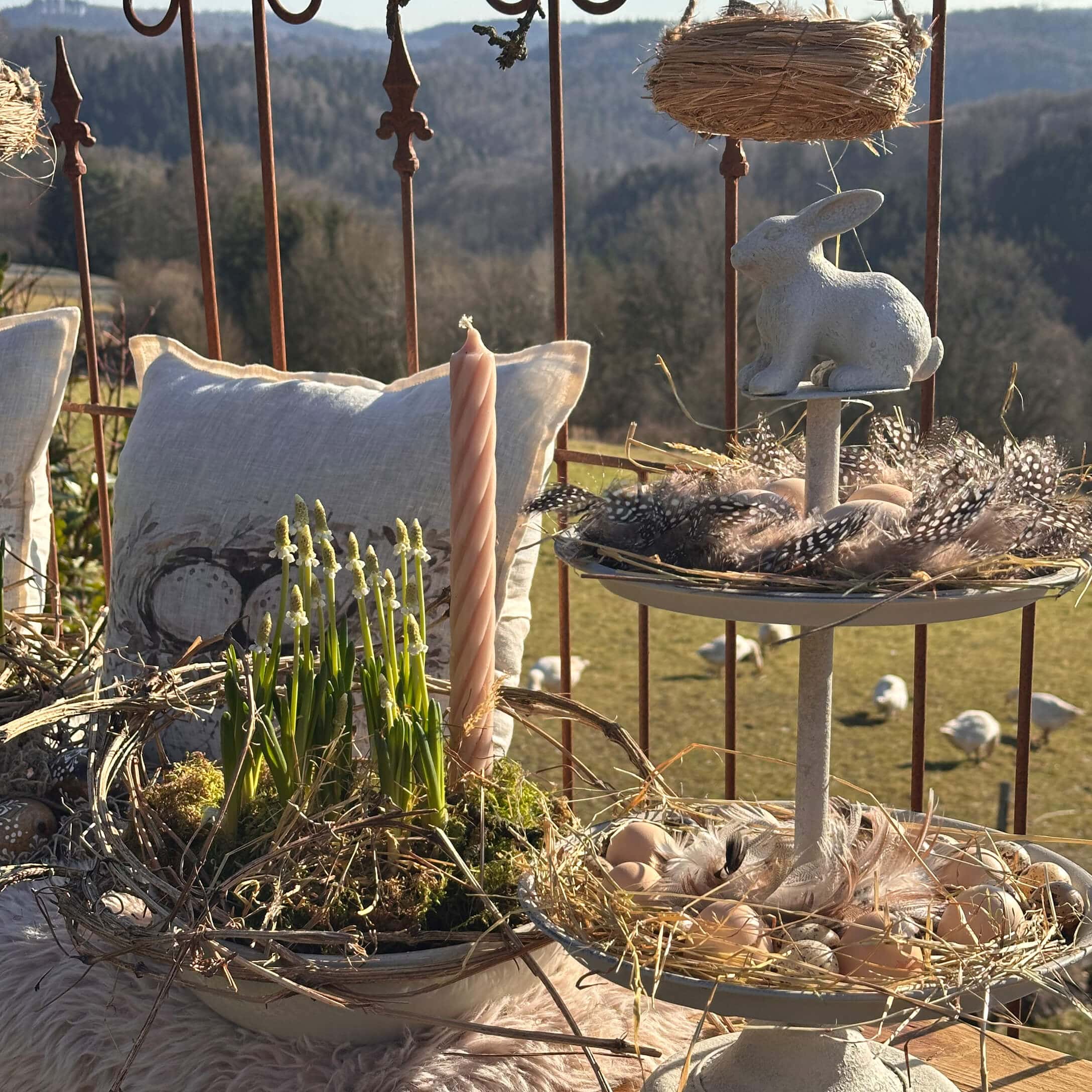 Decoración natural de Pascua con conejo blanco, plumas y vela sobre fondo rústico con cojines