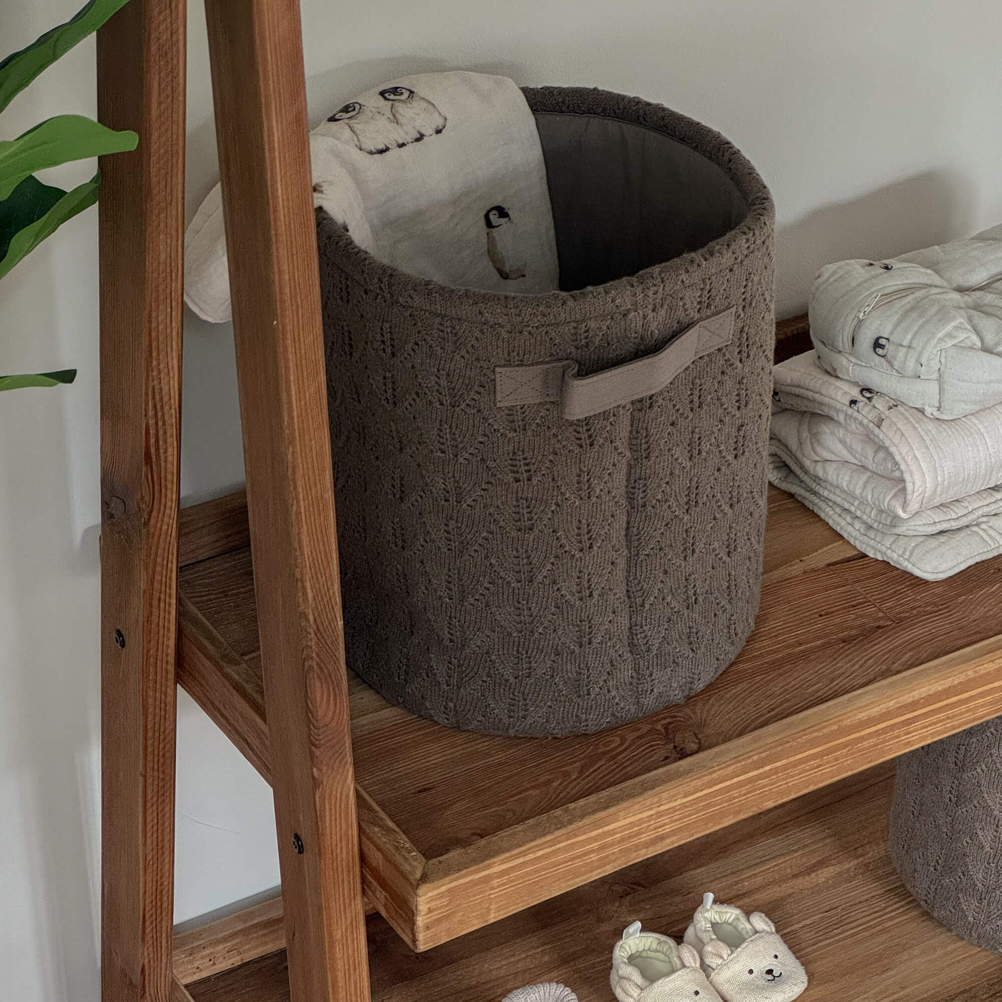 Cesta tejida marrón en estante de madera con tela suave y zapatillas de bebé beige