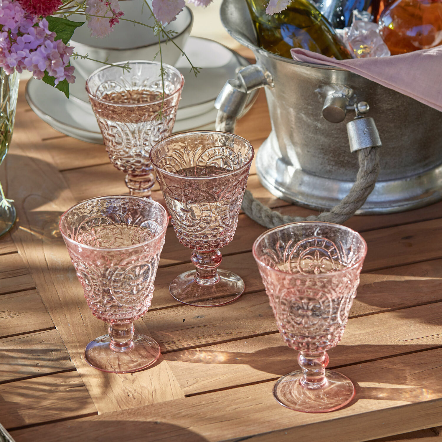 Set de 4 copas de vino Sarton Conjunto de cuatro copas rosas con relieve sobre mesa de madera, decoración de mesa elegante