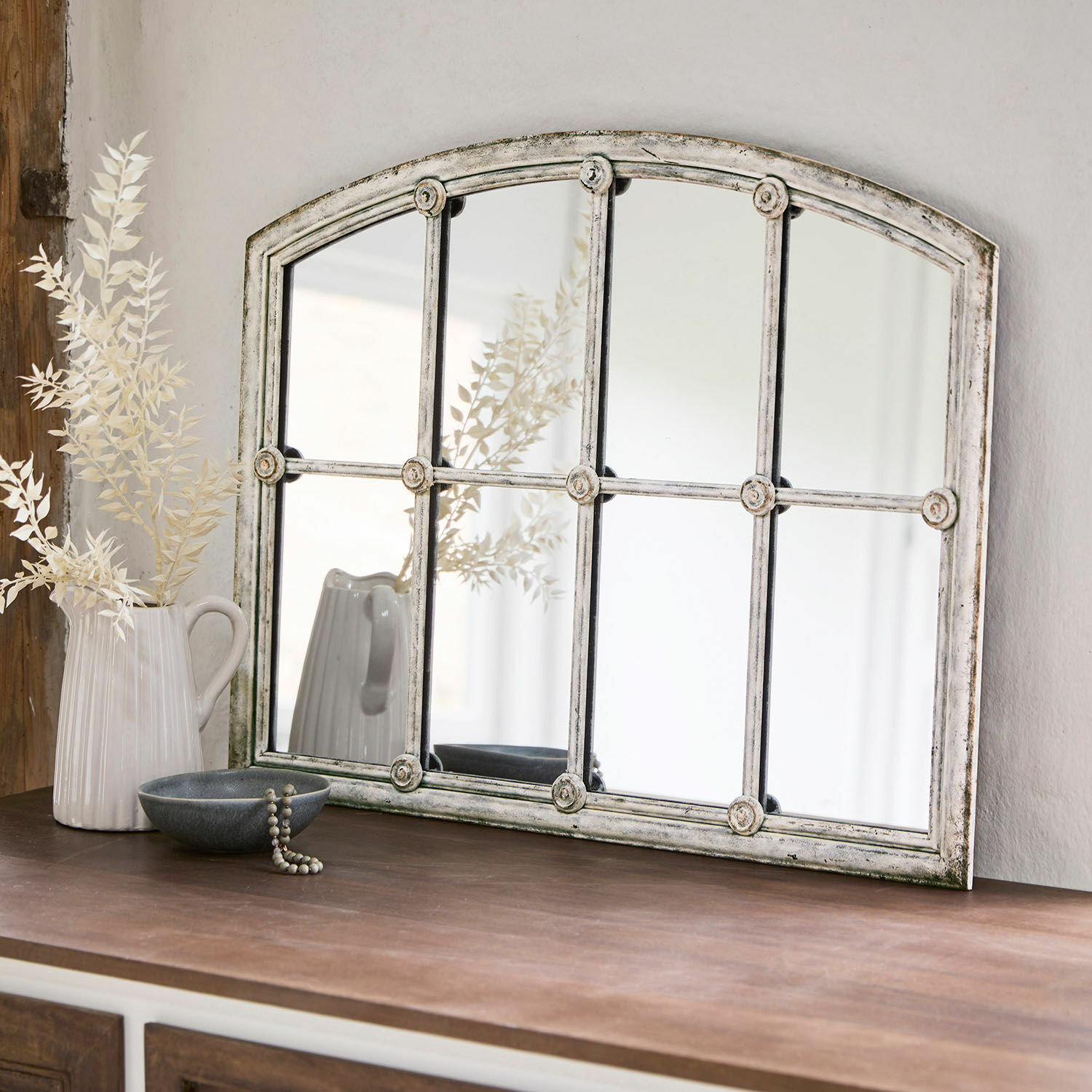 Espejo Tobiah Espejo rústico con marco metálico blanco envejecido sobre mueble de madera oscura