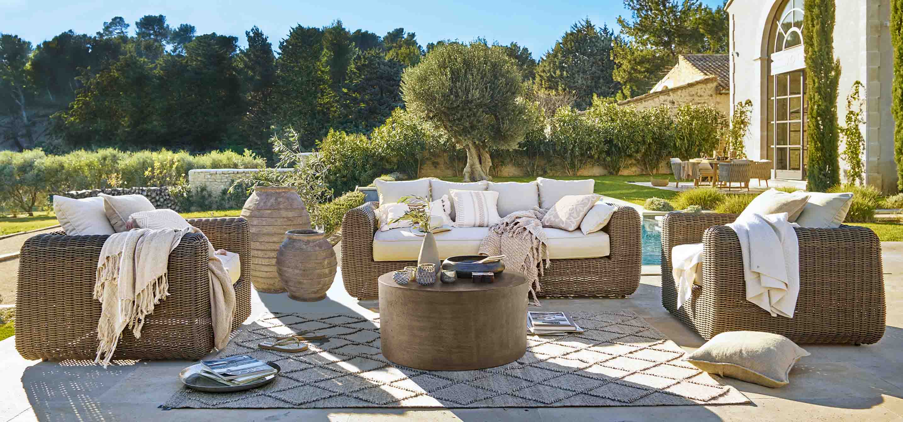 Conjunto de muebles de jardín de ratán marrón con cojines crema y mesa de centro redonda en terraza soleada