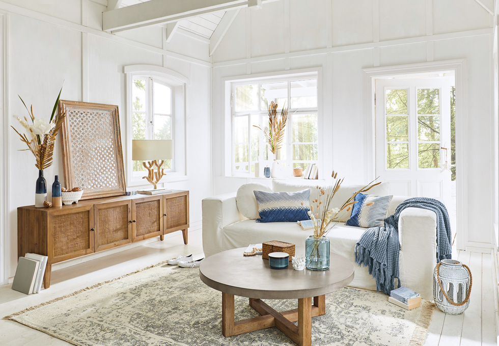 Sala luminosa estilo marítimo con sofá blanco, aparador de madera y detalles azules