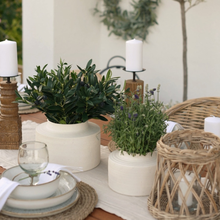 Macetas de cerámica blanca con plantas verdes sobre mesa de madera con candelabros naturales