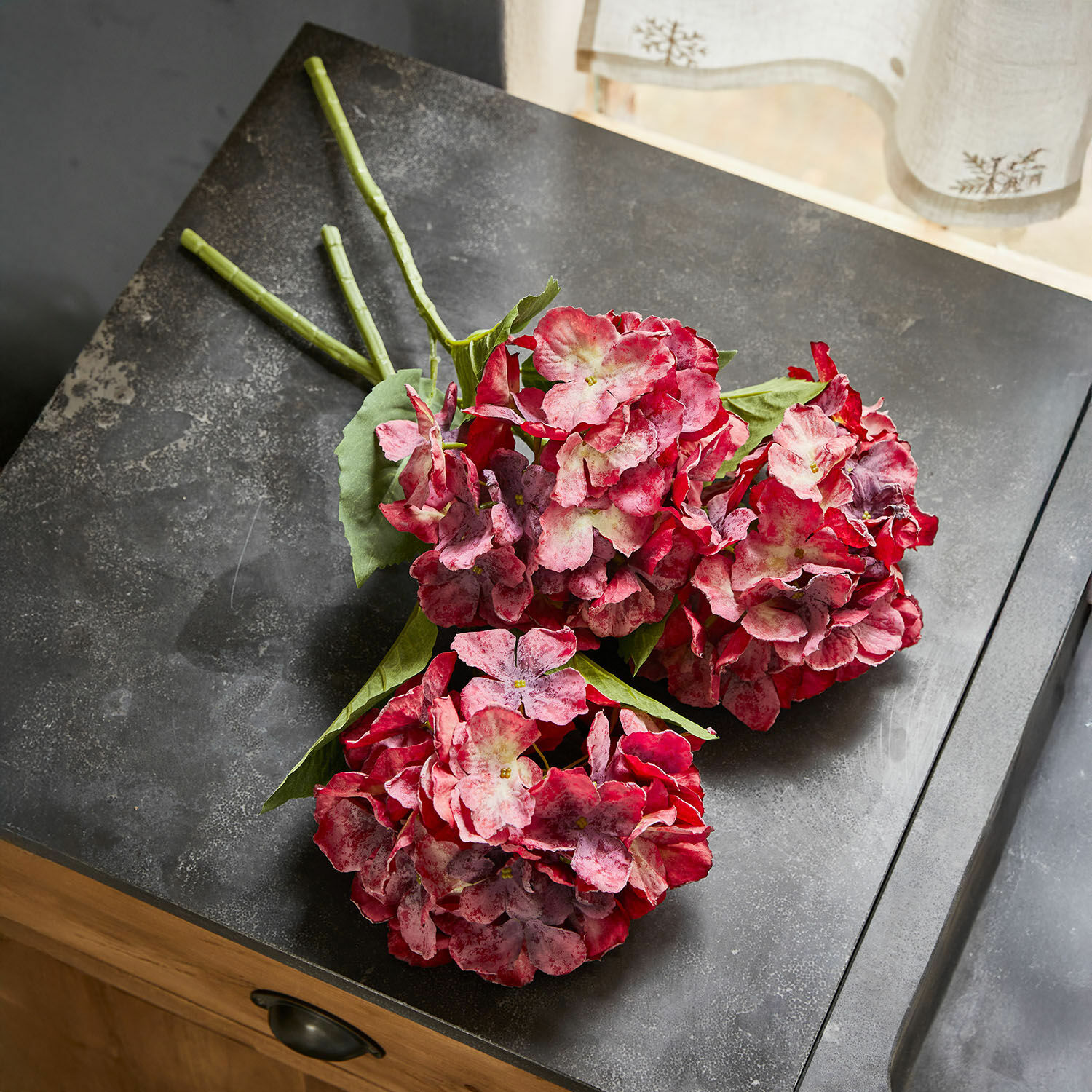 Set de 3 flores decorativas Virette Ramo de hortensias artificiales en tonos rojo y rosa con hojas verdes sobre superficie oscura