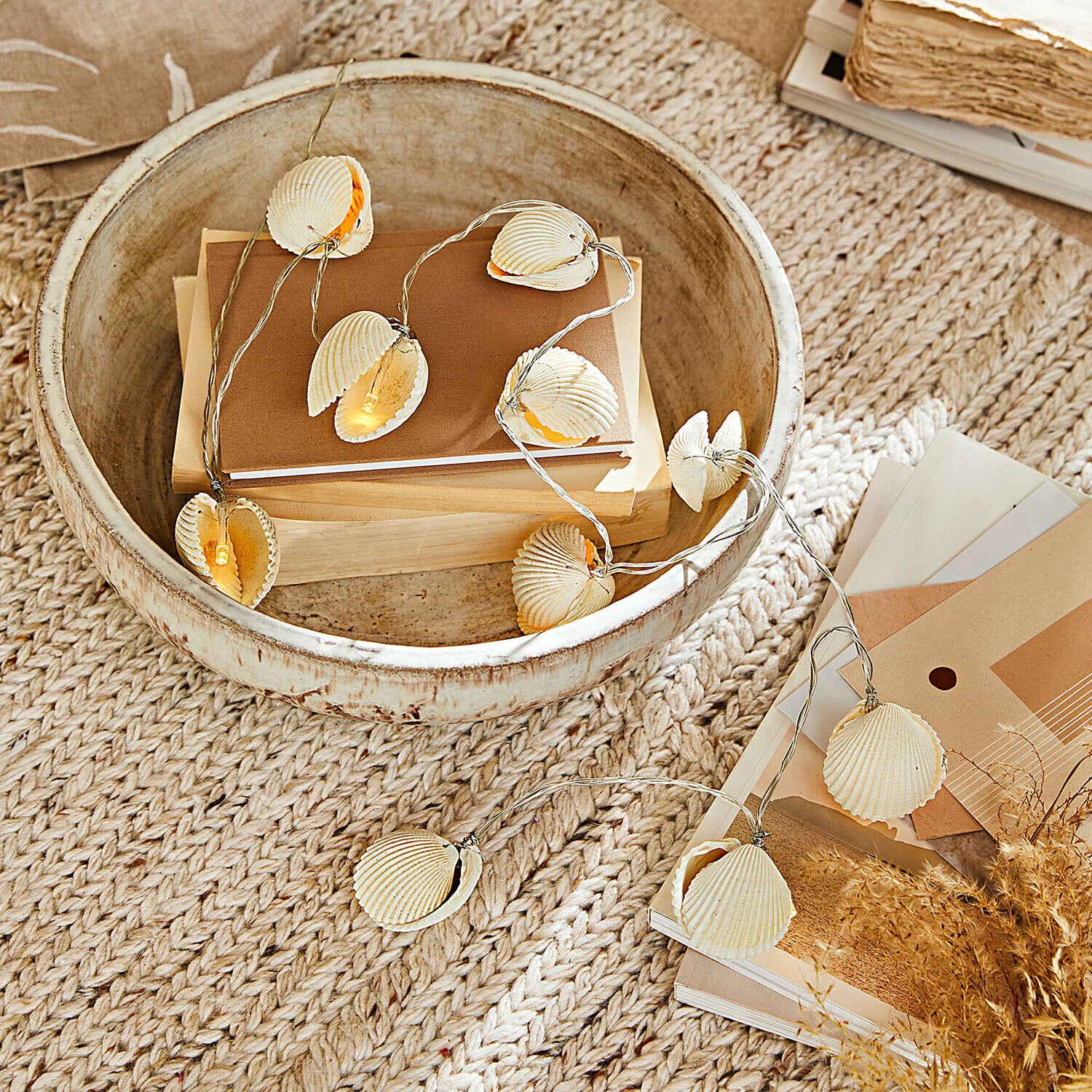 Luces de hada Havenor Guirnalda de luces con conchas naturales en tonos beige sobre cuenco de madera con libros y decoración