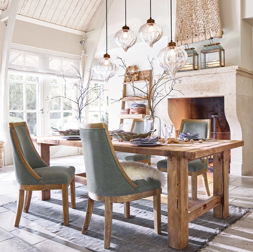 Comedor con mesa de madera maciza y sillas tapizadas grises, lámparas colgantes de vidrio decorativas