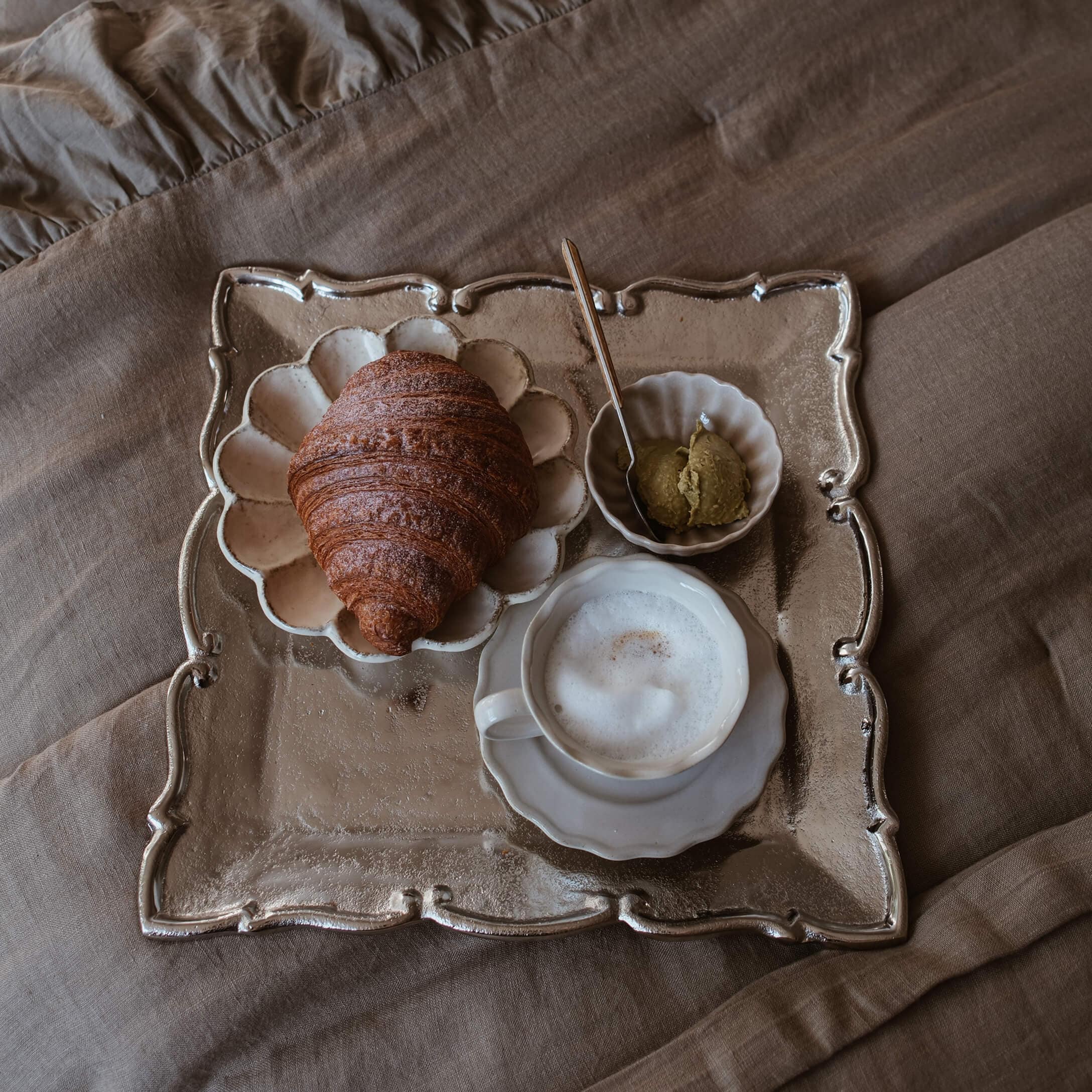 Bandeja con croissant, café con espuma y pasta sobre tela beige, estilo slow living