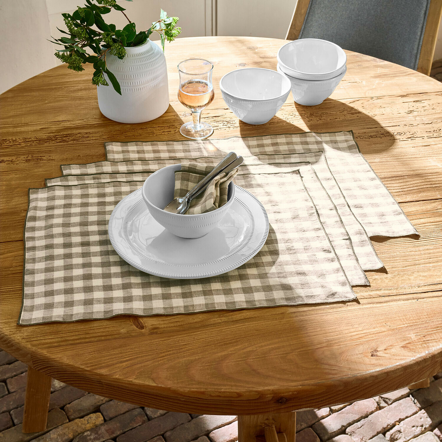 Set de 4 manteles individuales Marrowby Cuencos y plato de cerámica blanca sobre mesa de madera con manteles individuales de lino a cuadros beige