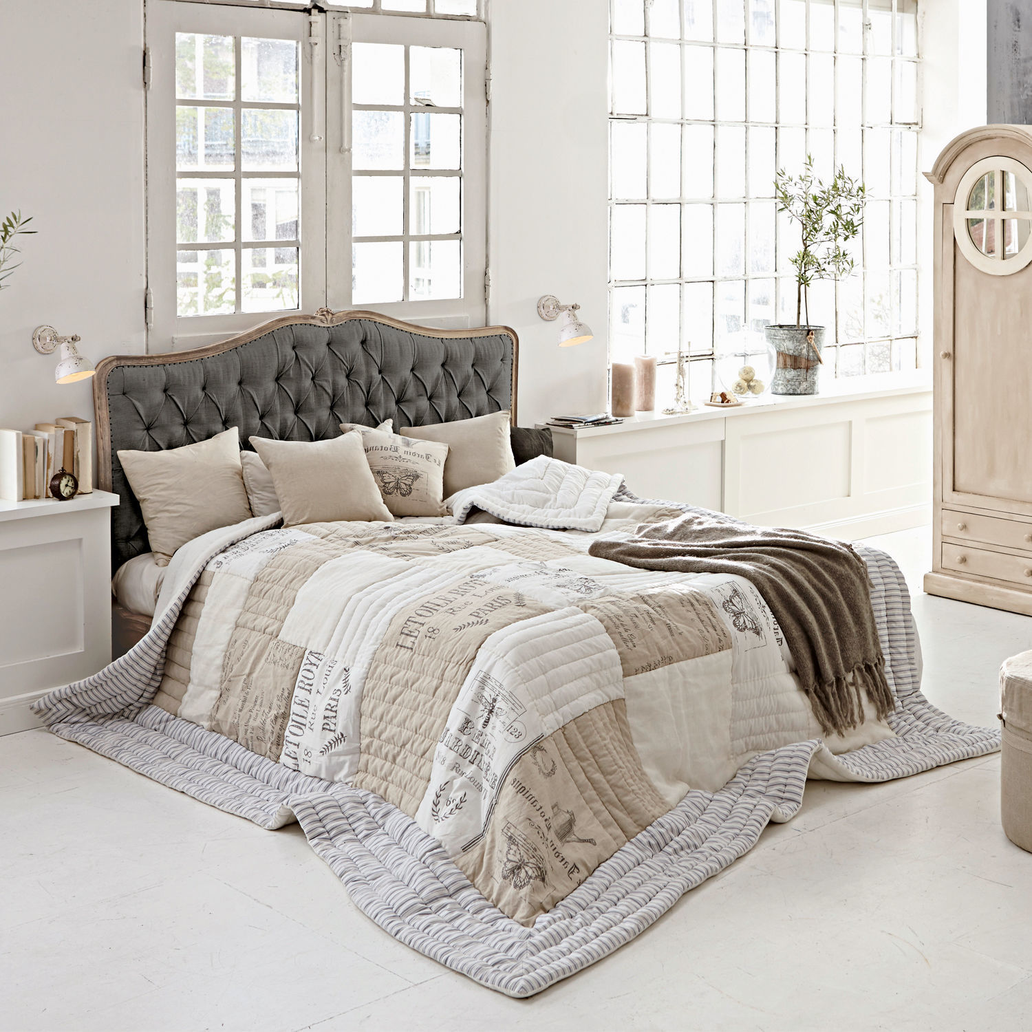 Cama Declaire Dormitorio acogedor con cama con cabecero gris acolchado y colcha beige y blanca con estampado vintage