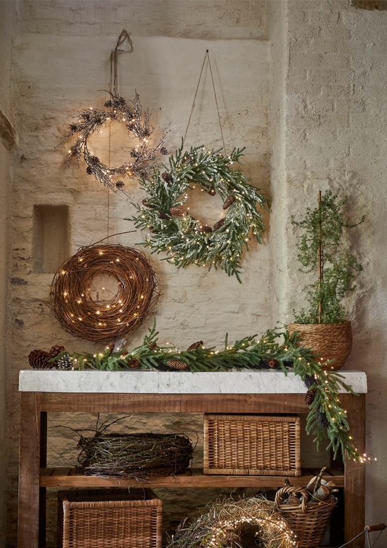 Coronas navideñas decorativas de ramas y luces colgadas en pared de piedra y mesa de madera con mármol