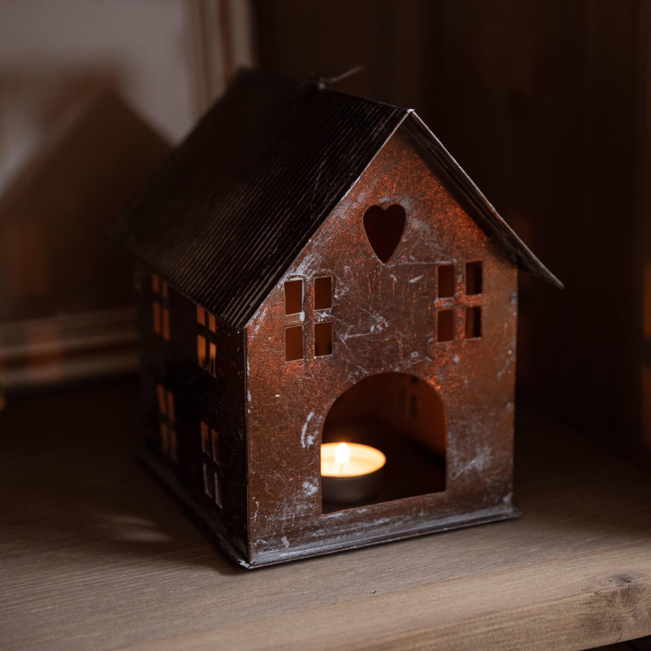 Farol de metal con forma de casa, recorte de corazón y vela encendida en estante de madera