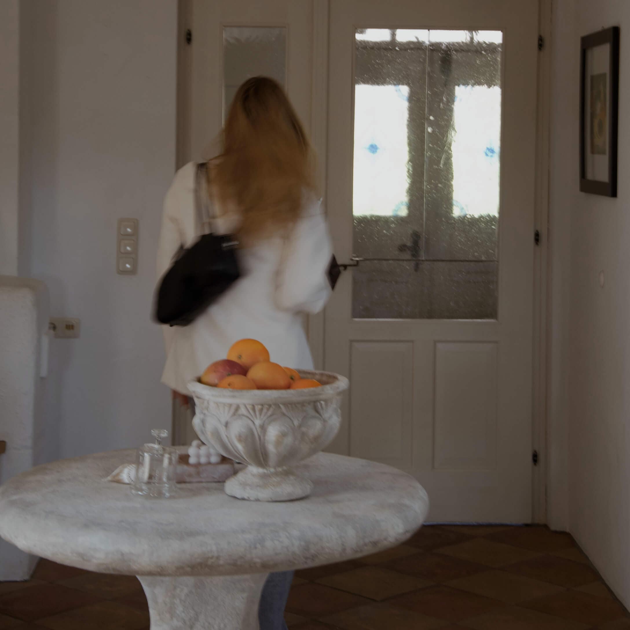 Cuenco decorativo de piedra con naranjas sobre mesa redonda en interior luminoso con puerta acristalada.