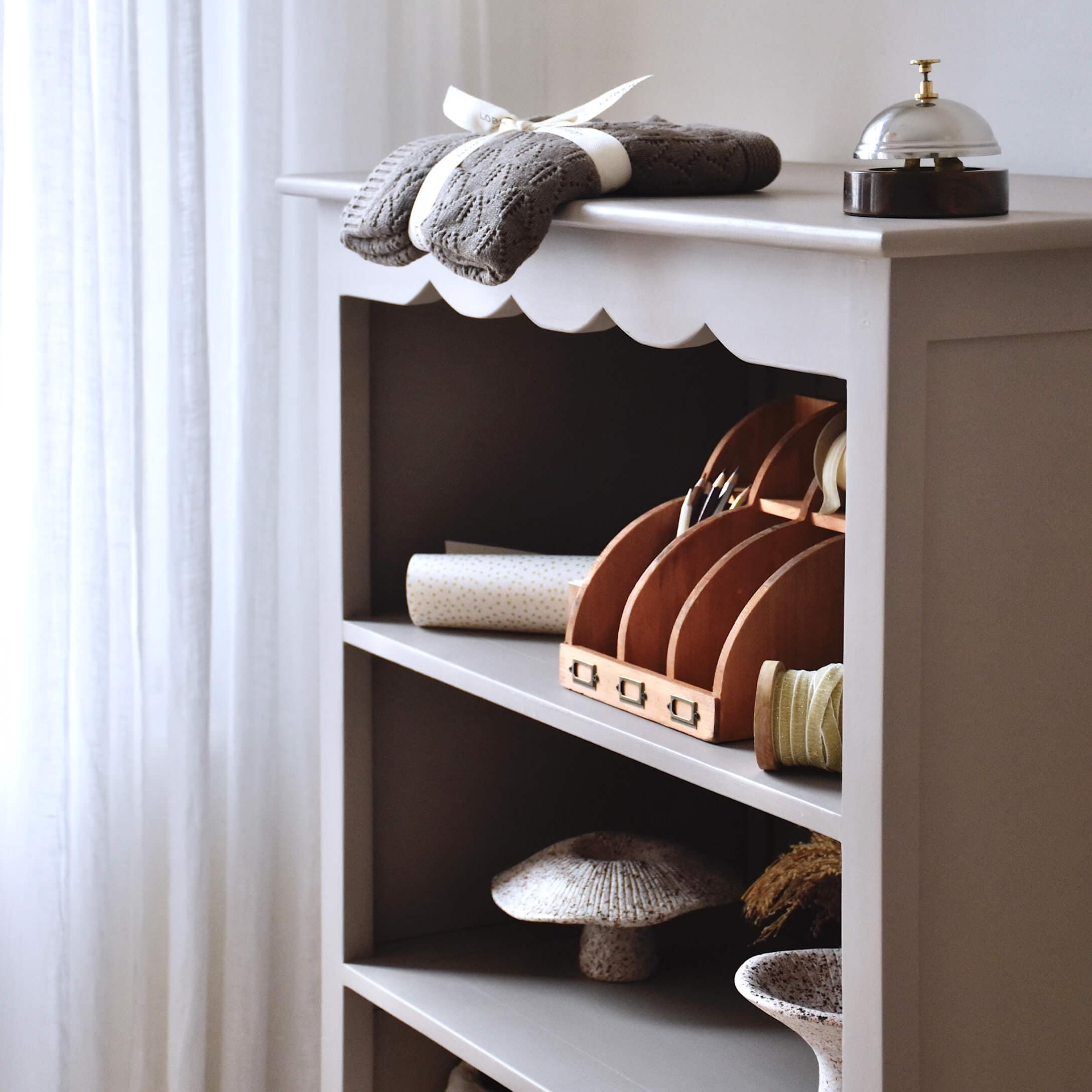 Estantería de madera gris con objetos decorativos y tela de punto gris encima
