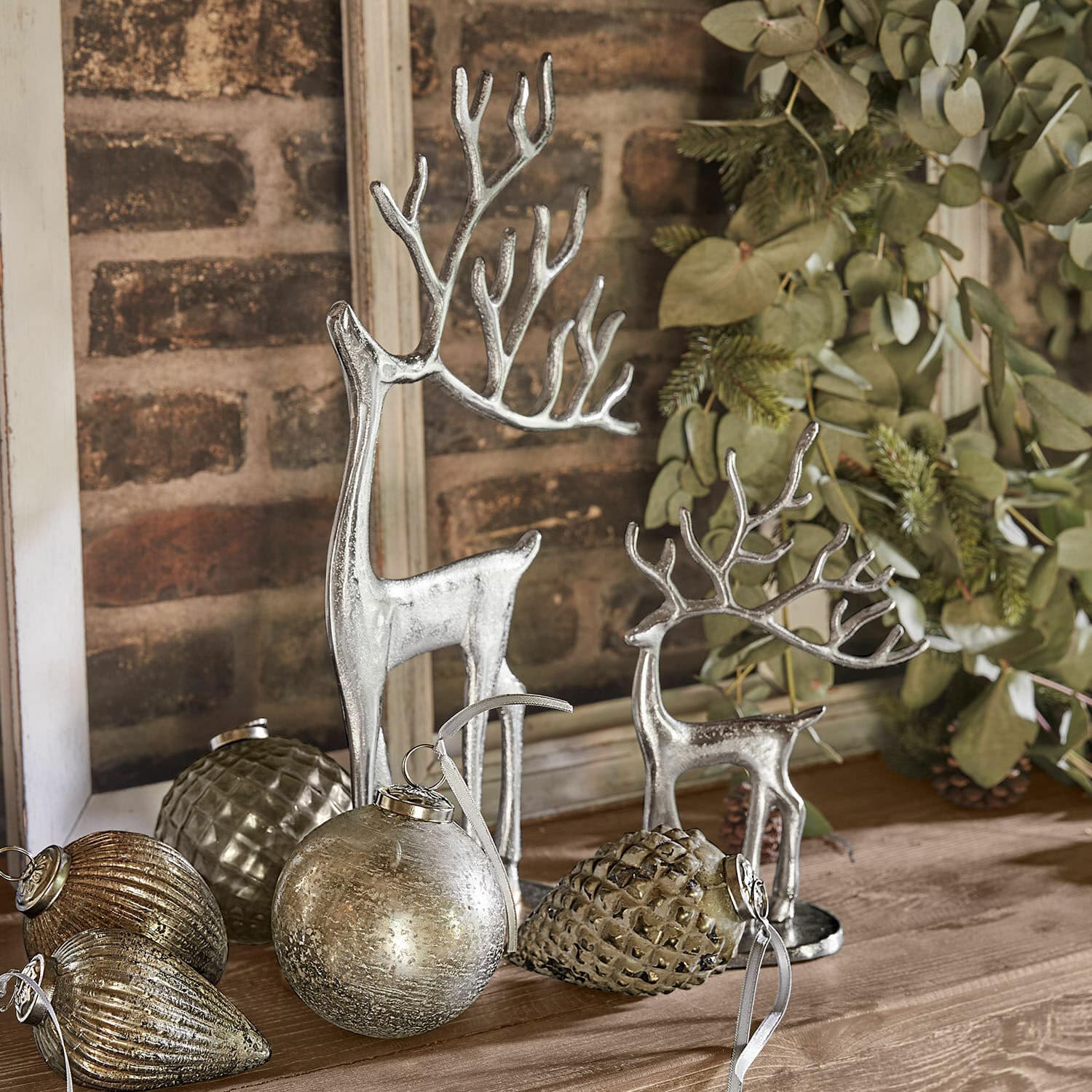 Figuras de renos plateados y adornos navideños sobre mesa de madera con ramas verdes
