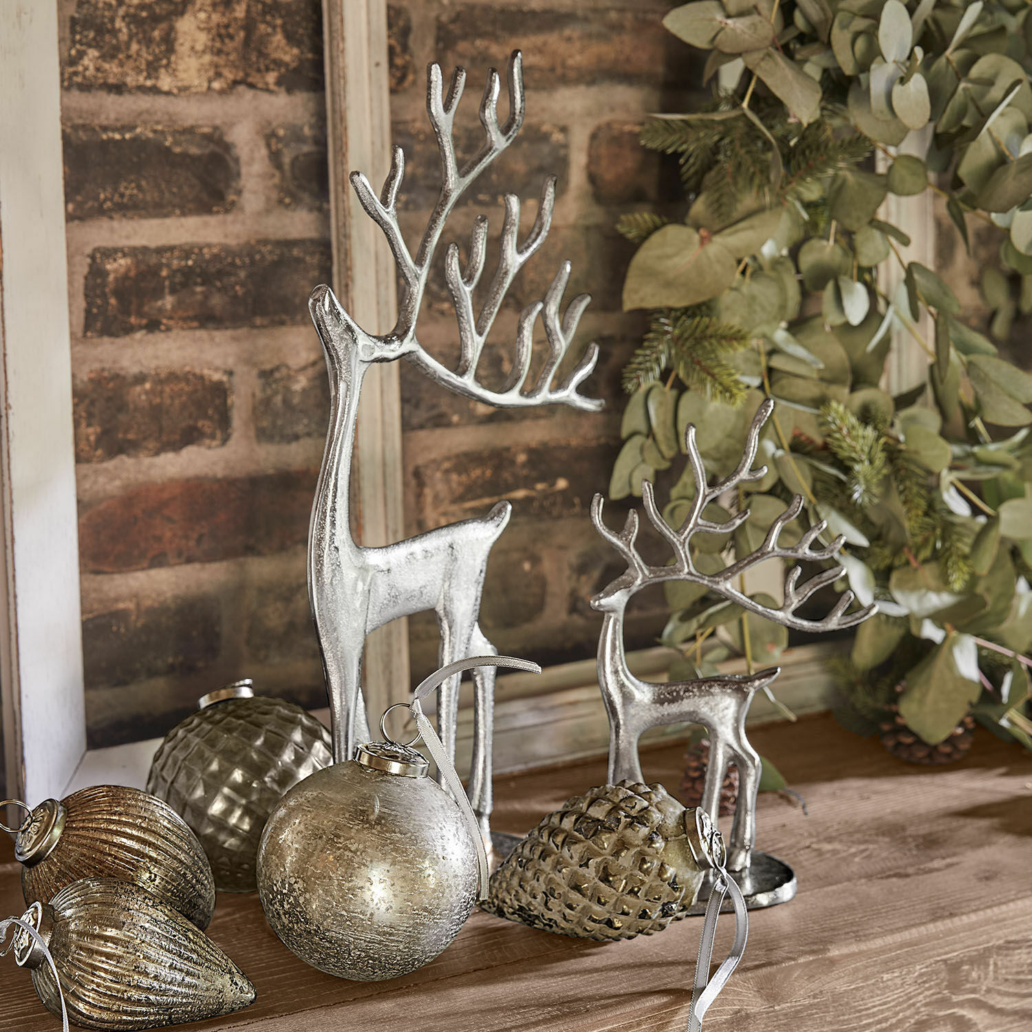 Set de 2 renos decorativos Zerlay Figuras de renos plateados y adornos navideños sobre mesa de madera con ramas verdes