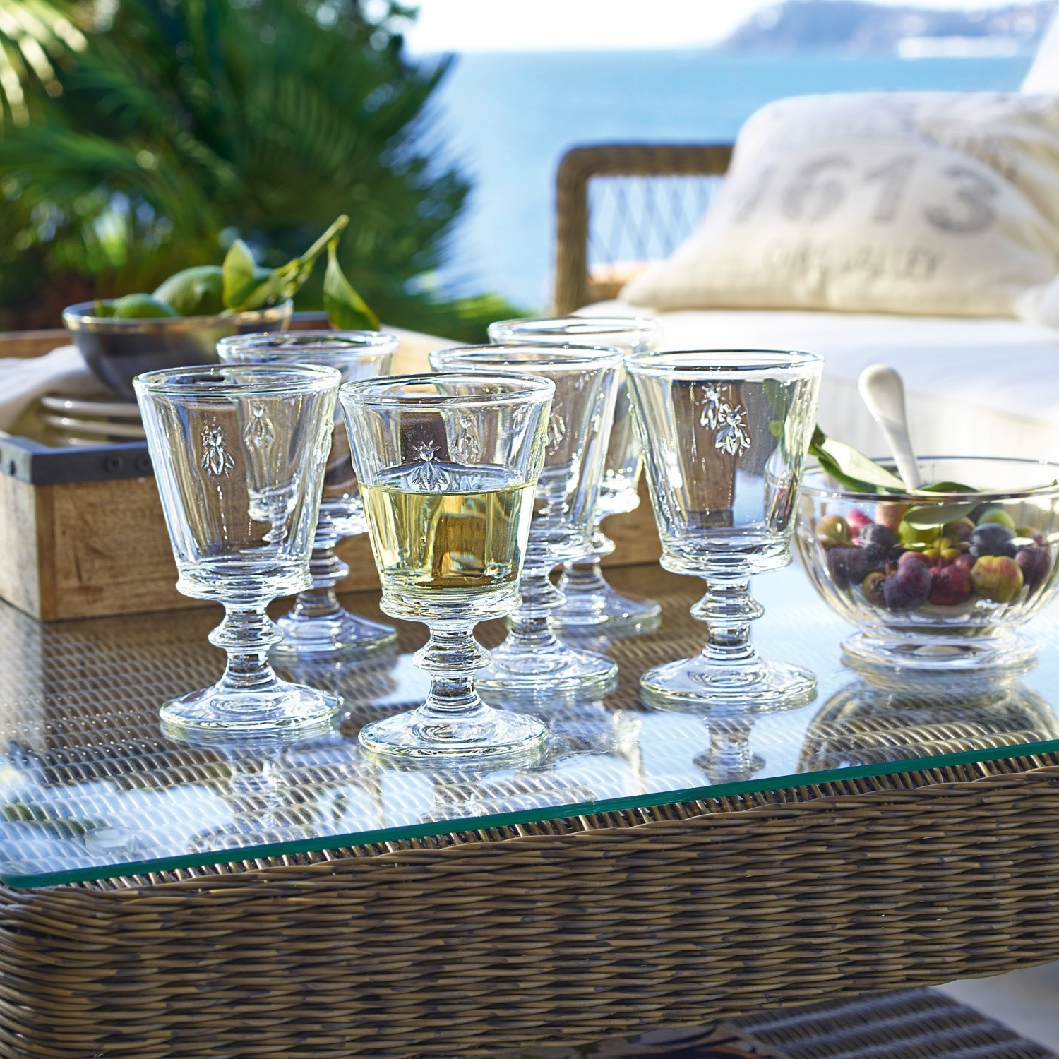 Set de 6 copas de vino Puttigny Conjunto de seis copas de cristal con motivo de insectos sobre mesa de cristal en terraza con vistas al mar