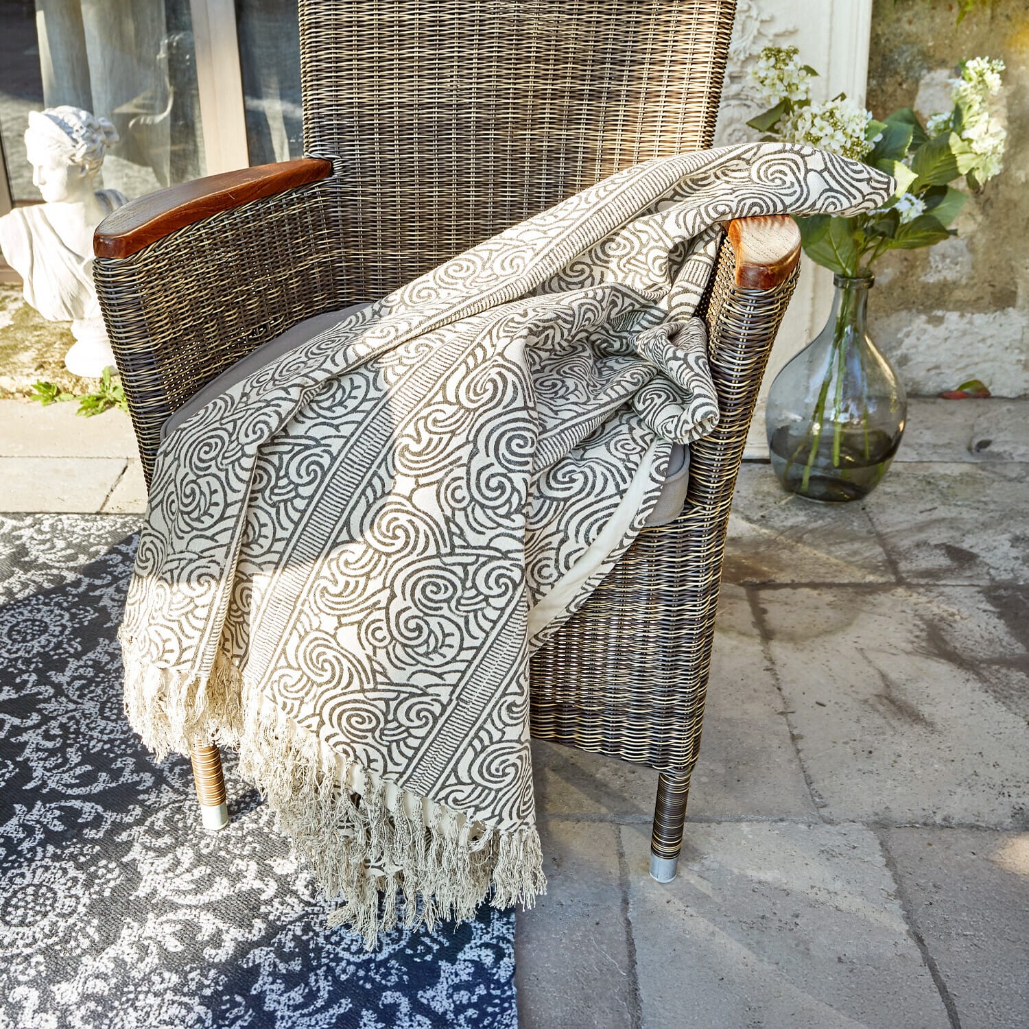 Manta Ensis Manta beige con patrón y flecos sobre silla de mimbre, decoración para hogar y jardín