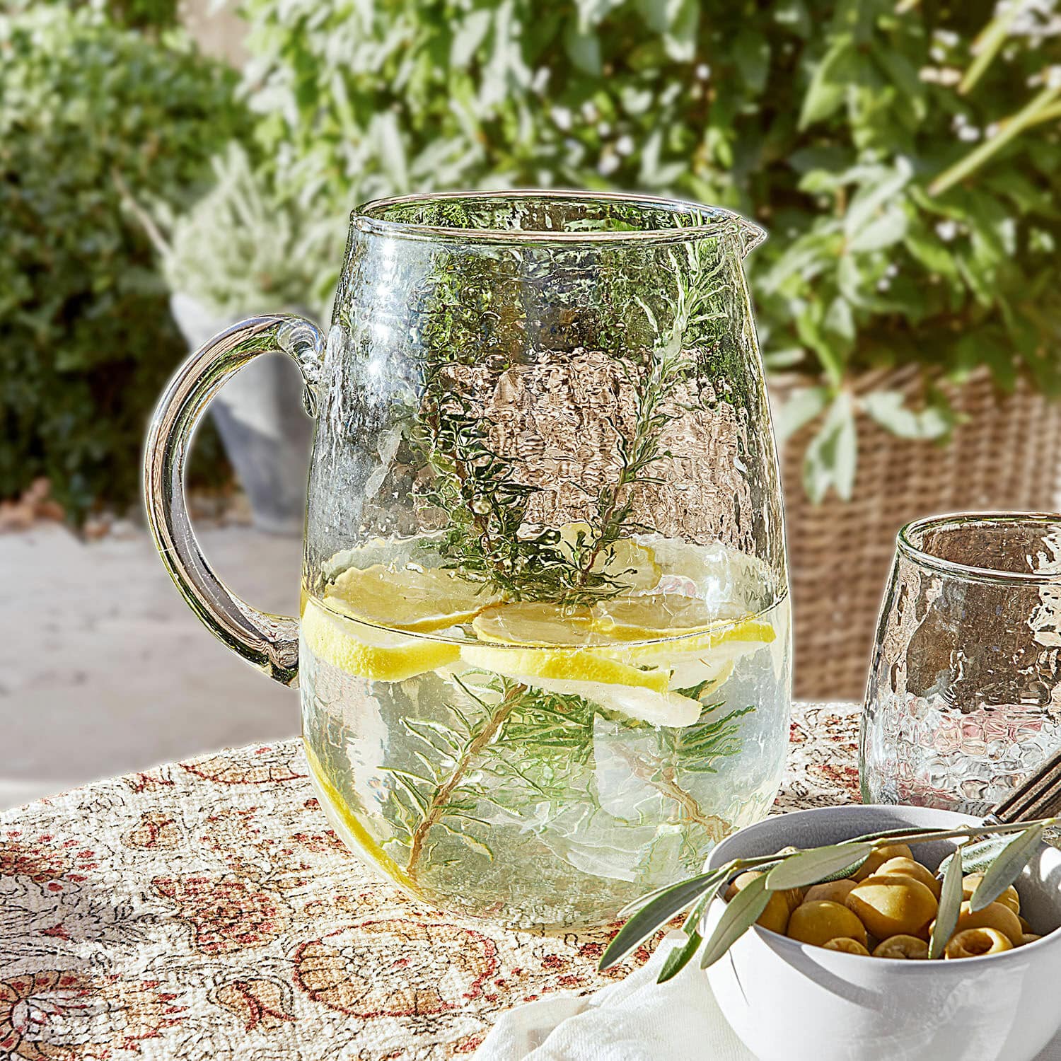 Jarra Rezay Jarra de vidrio con agua, limón y hierbas sobre mantel decorativo, bebida refrescante de verano