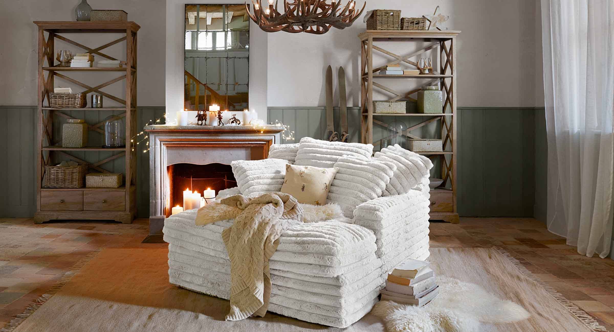 Sillón blanco de material suave estilo chalet en salón con chimenea y estanterías de madera rústica