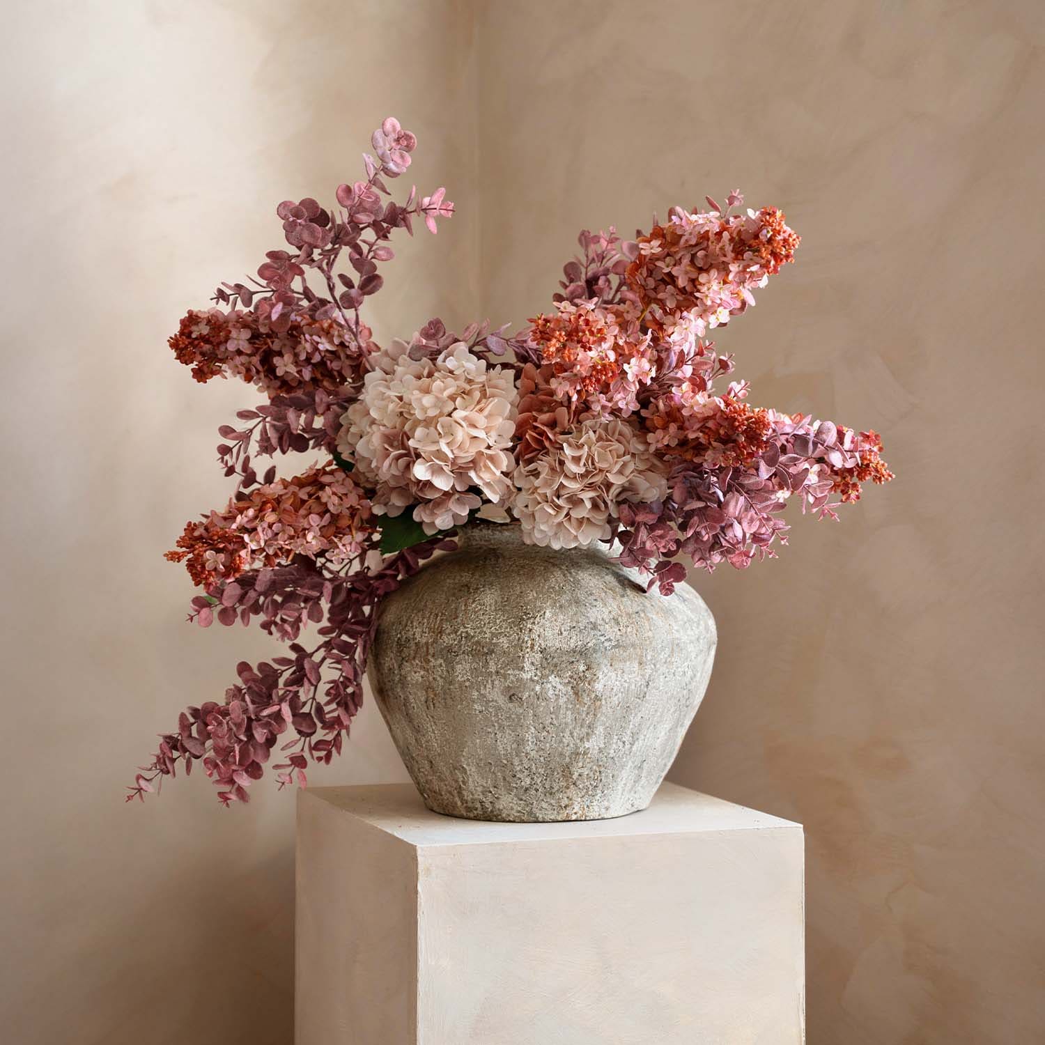 Jarrón rústico de piedra con ramo de flores decorativas rosas y beige para decoración interior