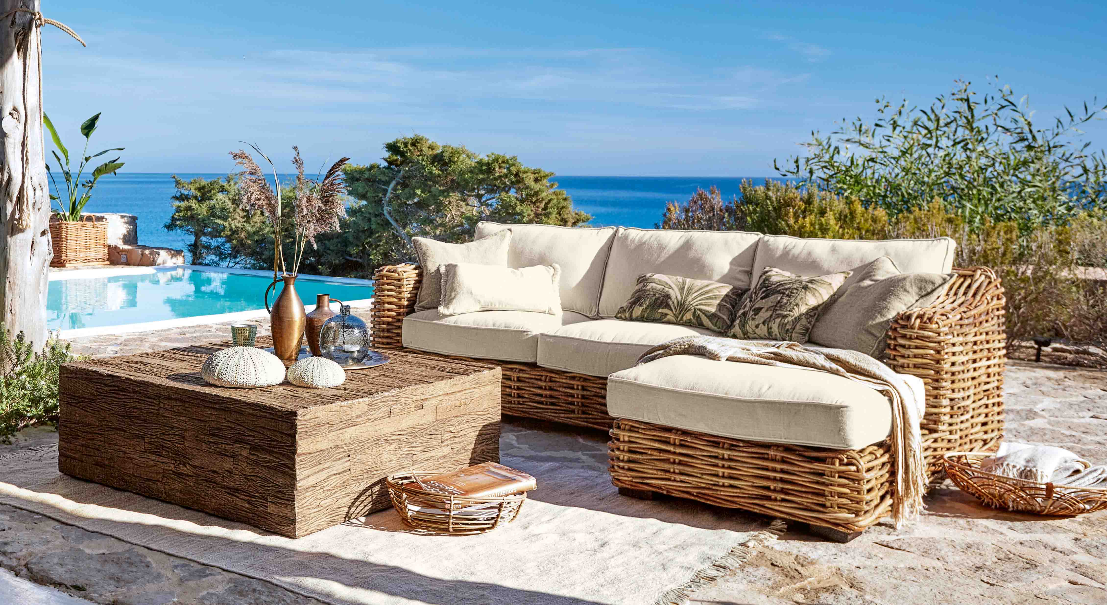 Conjunto de muebles de jardín de ratán con cojines crema junto a piscina con vista al mar