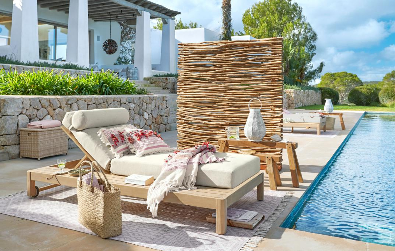 Tumbona de madera clara con cojín crema y biombo decorativo junto a la piscina en estilo marítimo