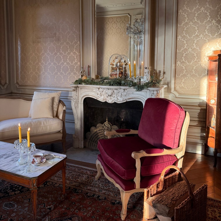 Salón clásico con sillón burdeos de madera y mesa de mármol con velas encendidas