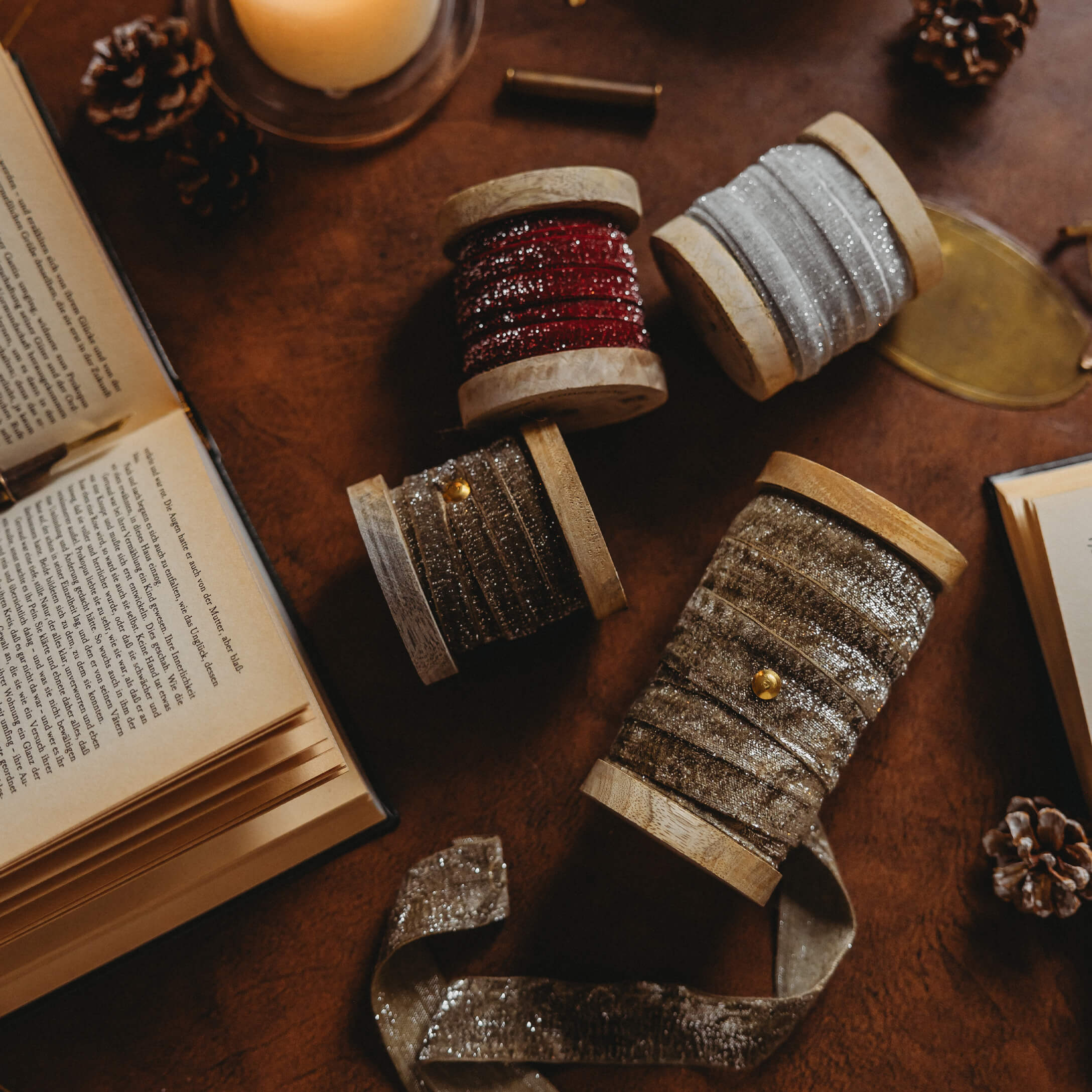 Carretes de madera con cintas brillantes rojas, plateadas y doradas sobre mesa con libros abiertos