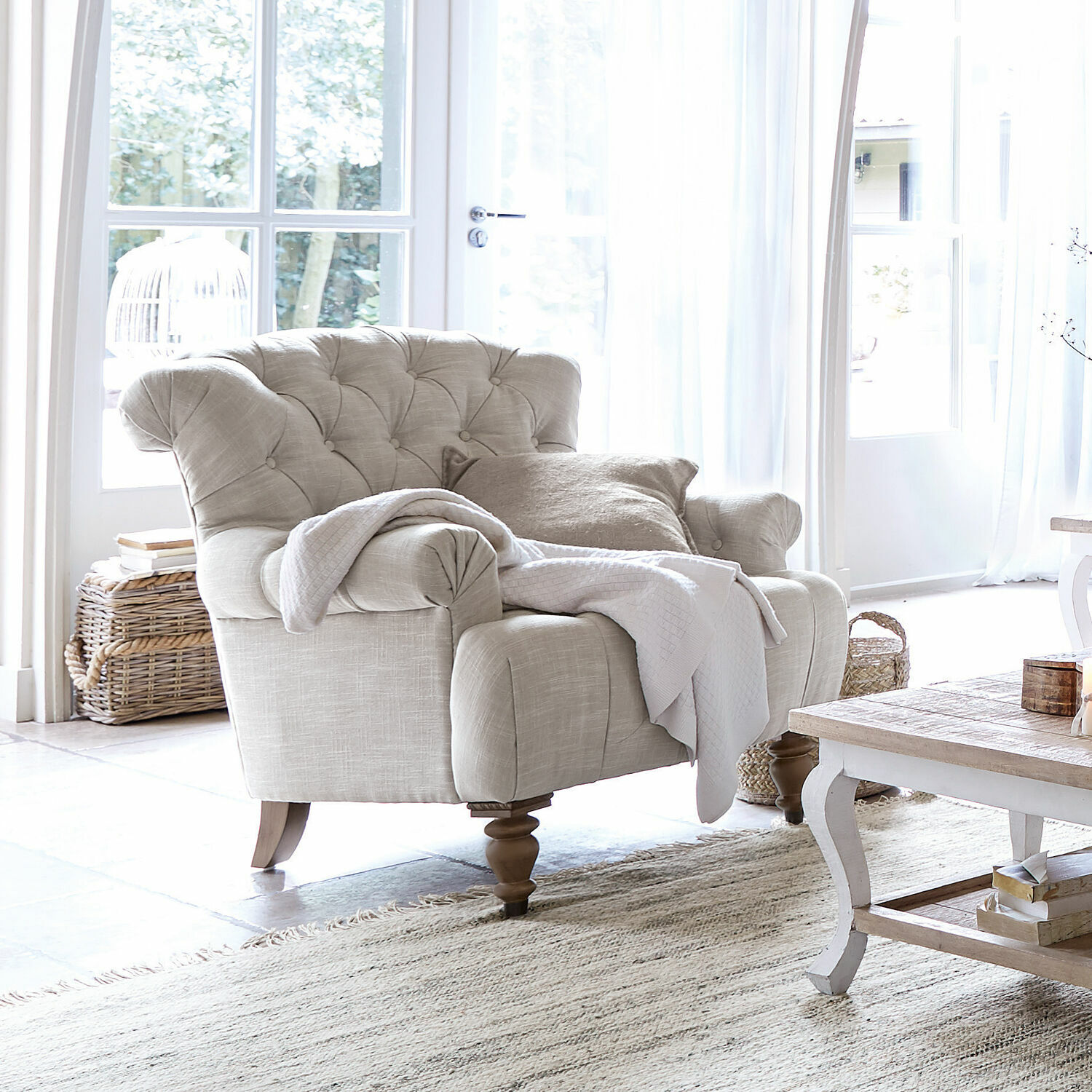 Sillón beige tapizado en tela con respaldo capitoné y patas de madera en sala luminosa