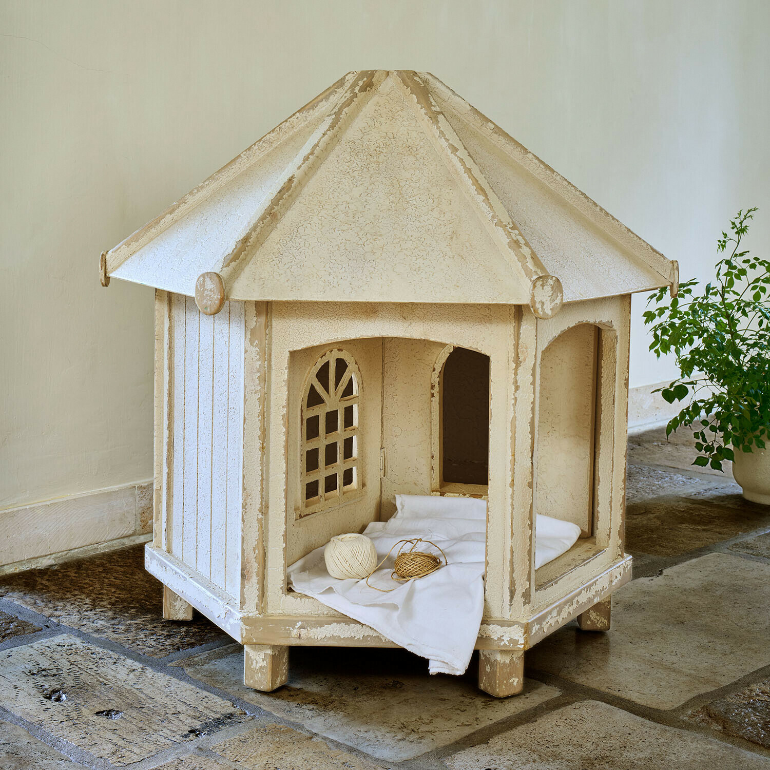 Caseta de jardín para gatos Alvérine Caseta para gato de madera beige con ventanas y cojín blanco sobre suelo de piedra