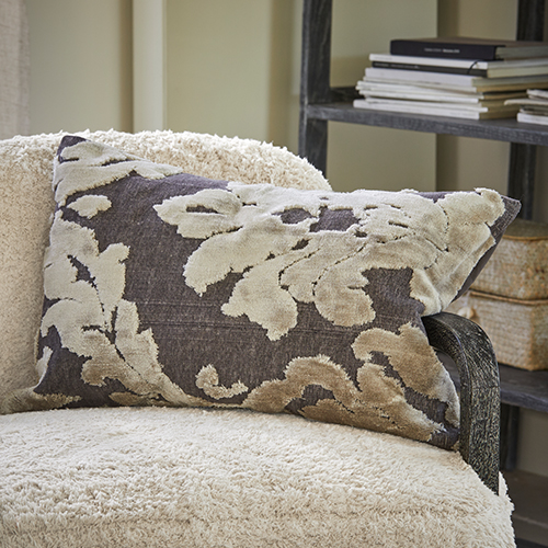 Cojín decorativo con diseño de hojas beige sobre fondo gris en sillón crema, textil para sala