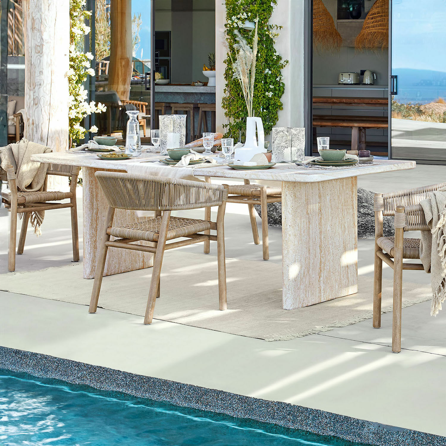 Mesa de comedor Yveline Mesa de comedor de piedra clara con sillas de madera trenzada junto a piscina en casa moderna