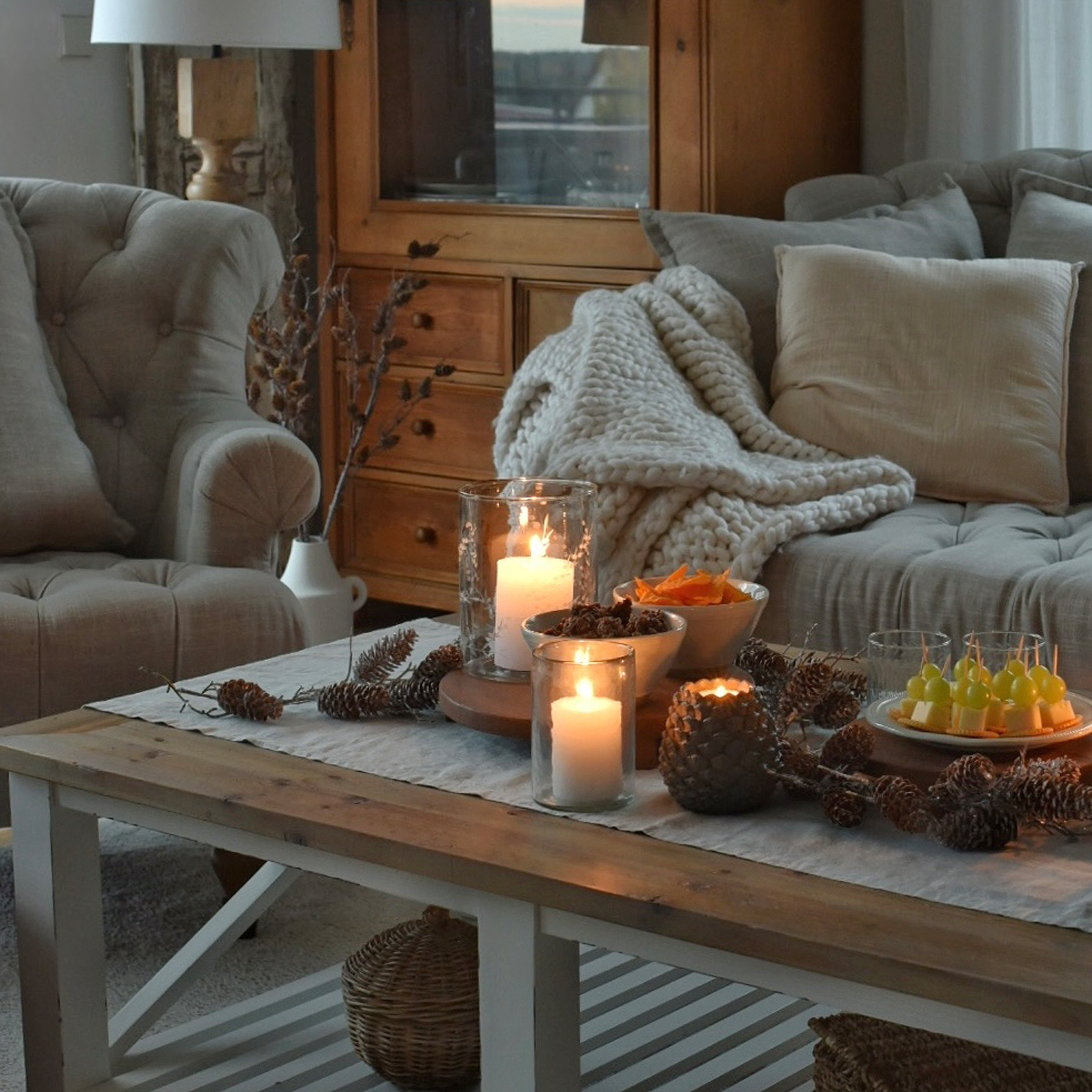 Sala acogedora con mesa de madera, velas encendidas y manta gris sobre sofá mullido