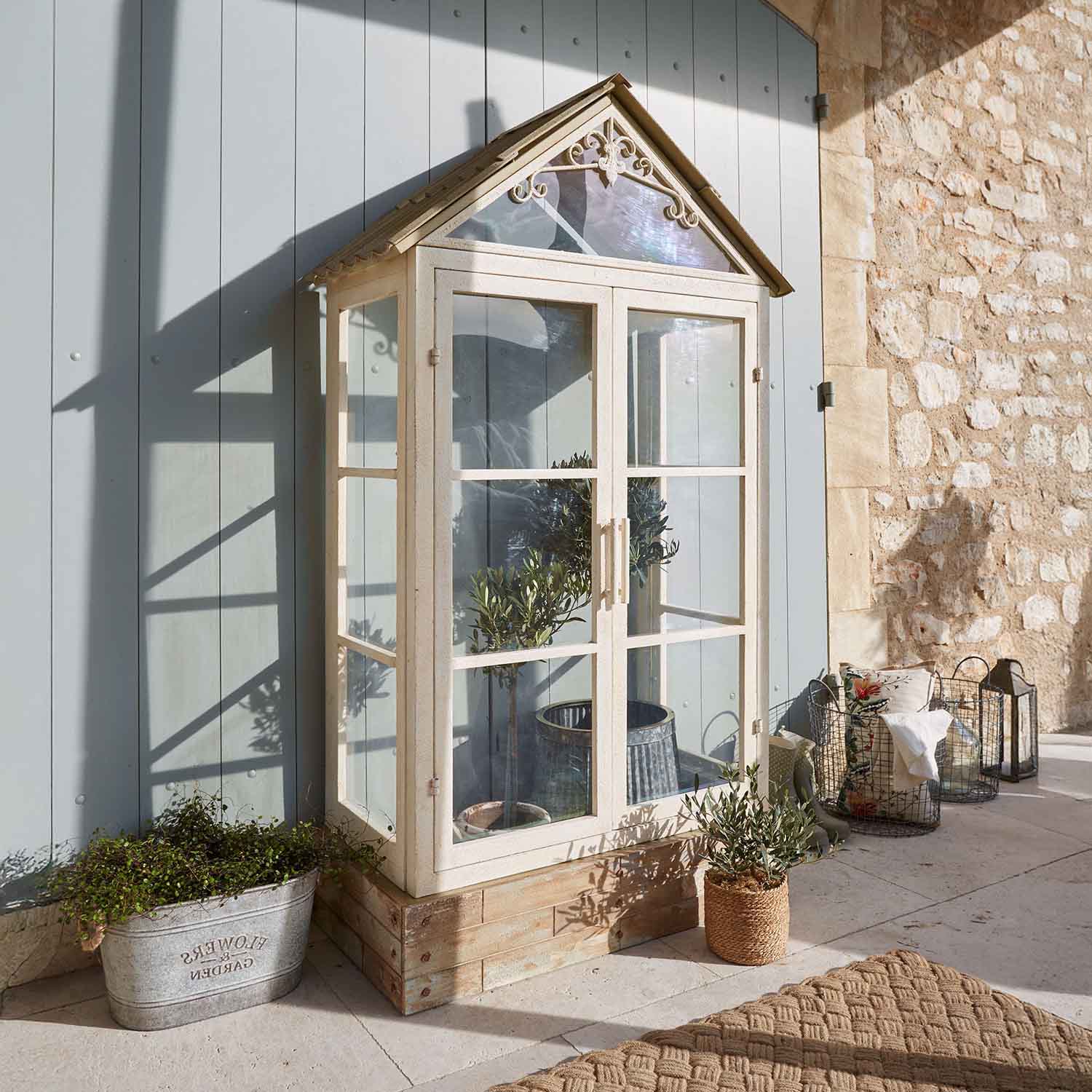 Invernadero pequeño de metal y vidrio color crema con plantas, decoración para terraza