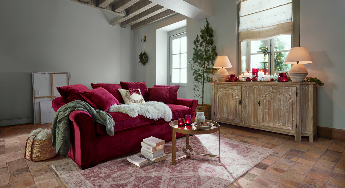 Sofá de terciopelo rojo con cojines y decoración navideña en sala acogedora con mesa de madera