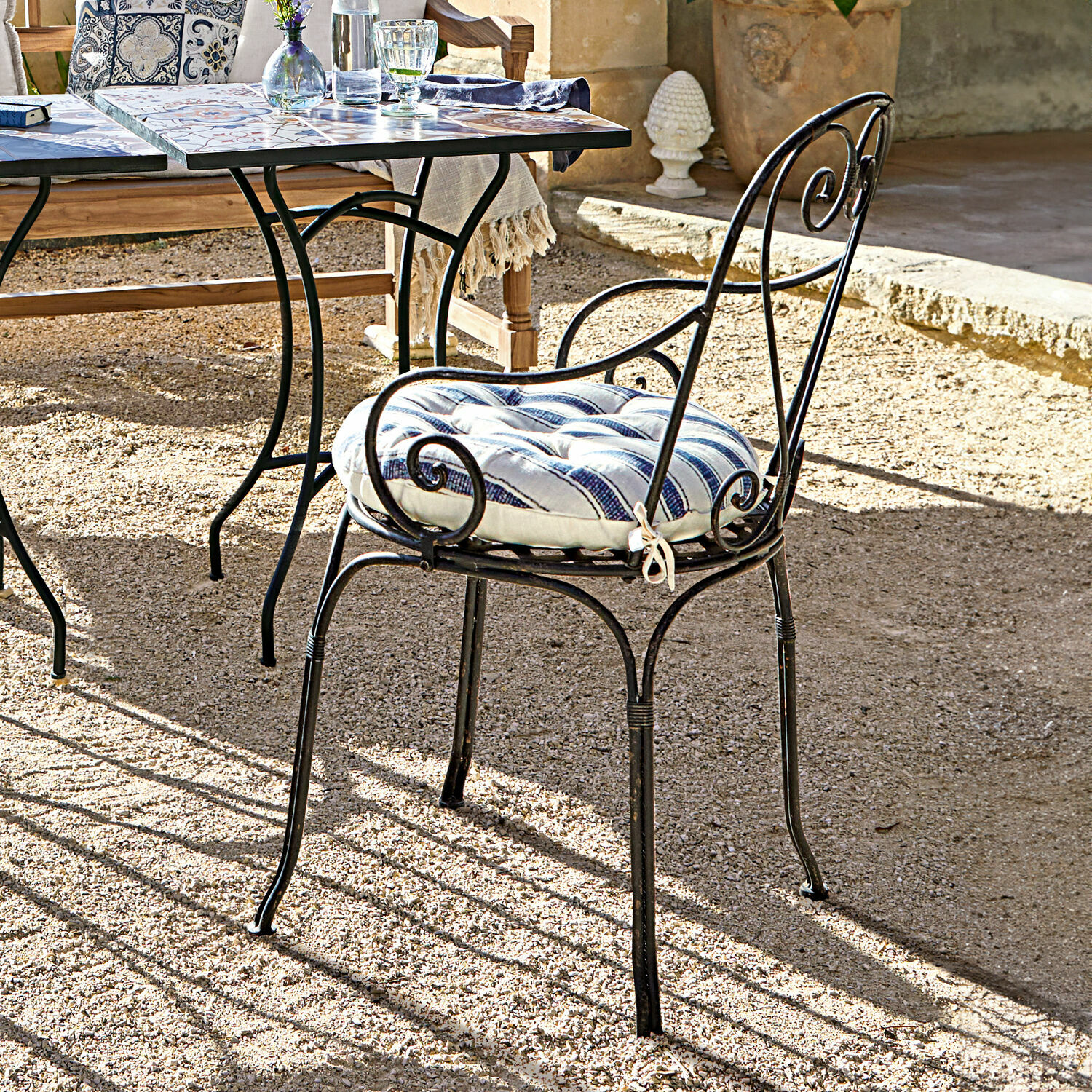 Silla de jardín de metal negro con cojín a rayas azules y blancas en terraza soleada