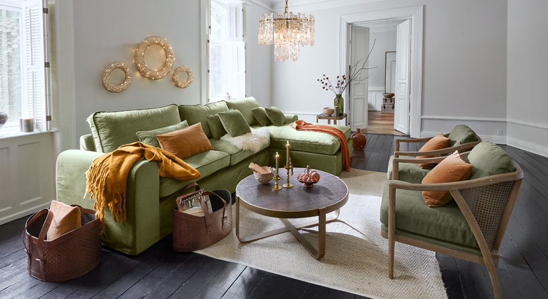 Sofá esquinero verde y dos sillones de madera en salón luminoso con mesa de centro y decoración