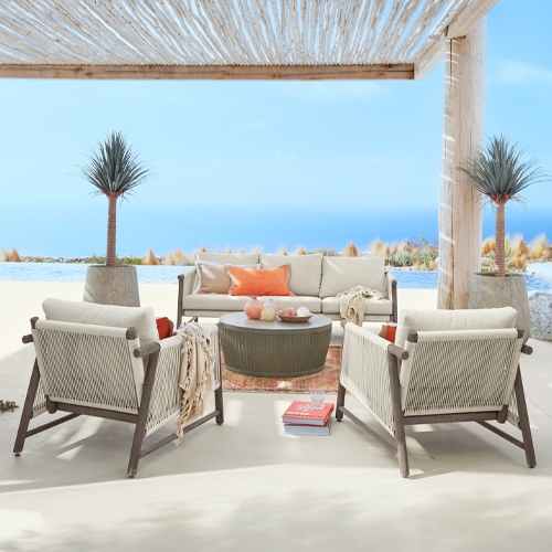 Conjunto de muebles de exterior con cojines beige y estructura de madera en terraza con vista al mar
