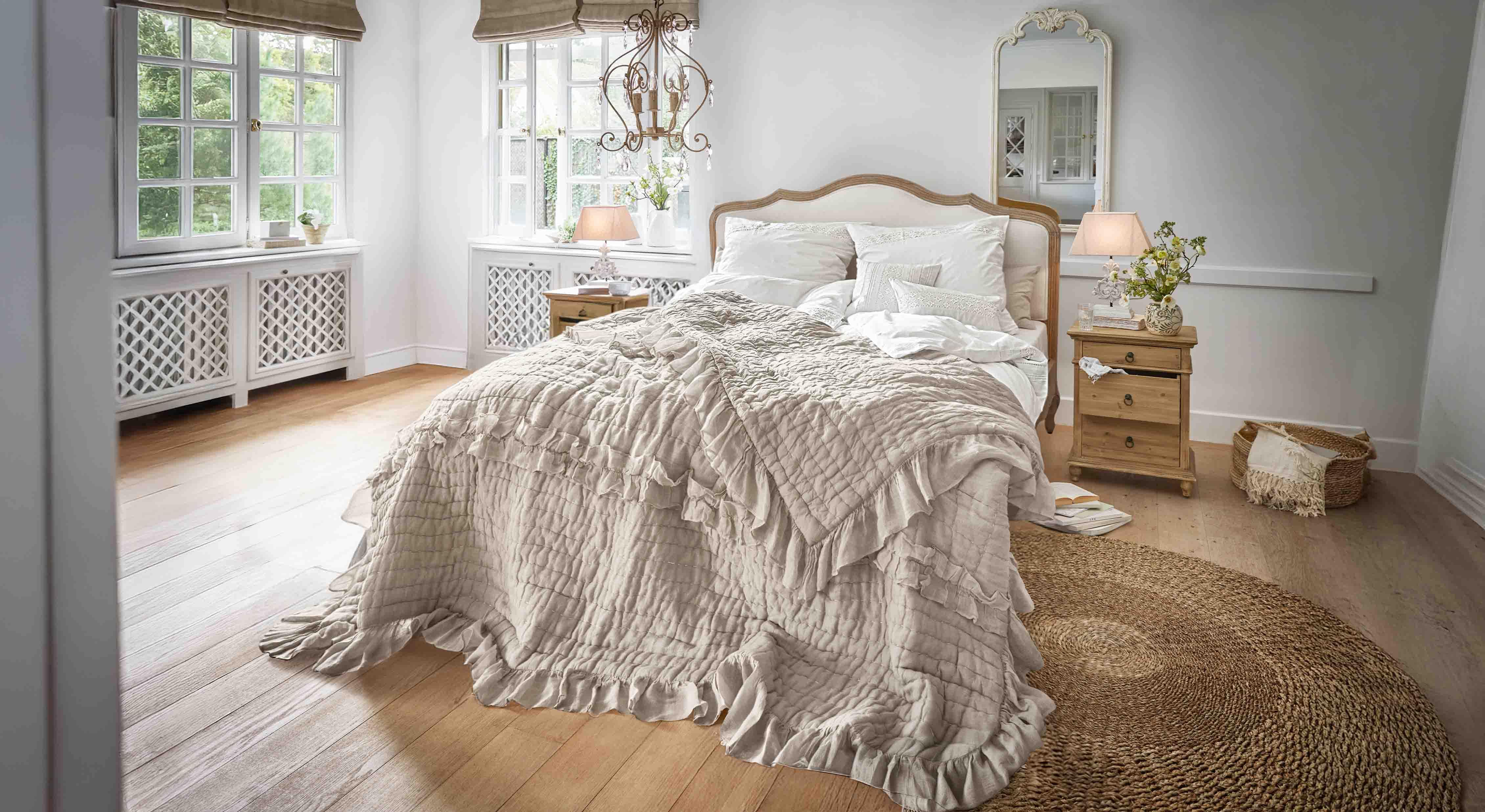 Dormitorio acogedor con cama cubierta por colcha beige con volantes y muebles de madera