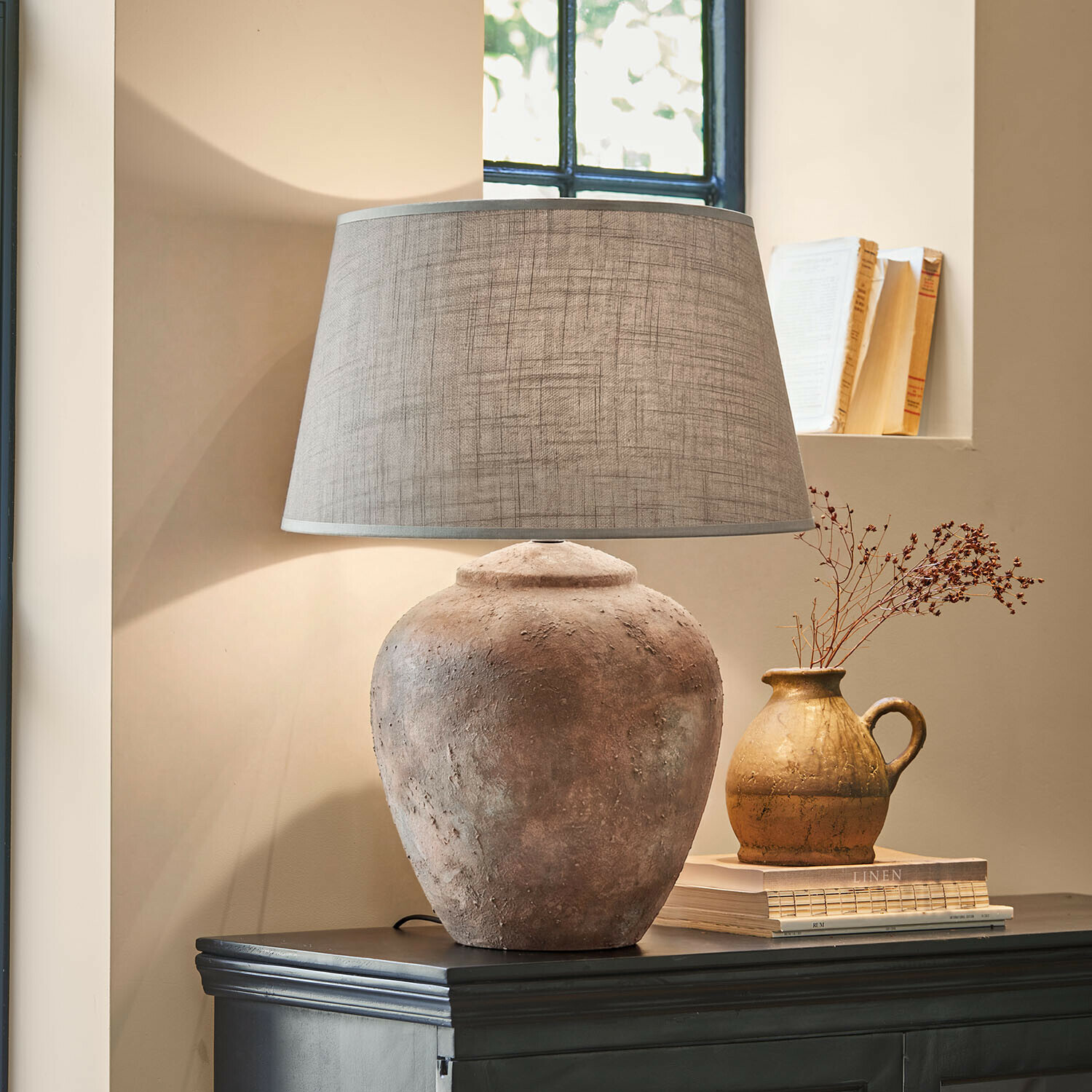 Lámpara de mesa Kelvador Lámpara de mesa con base de barro y pantalla gris sobre cómoda oscura en ambiente acogedor