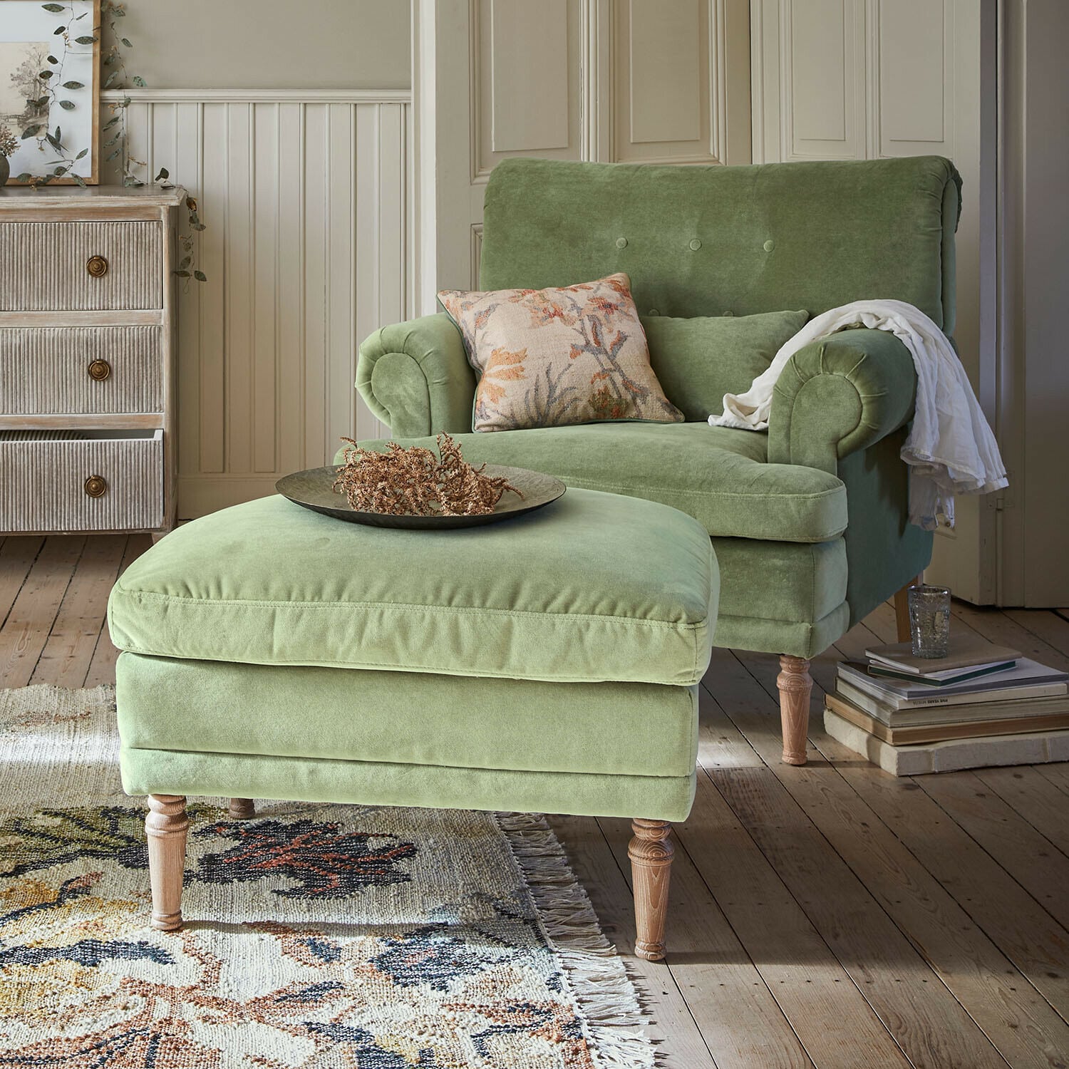 Sillón con reposapiés Éclat Émeraude Sillón verde de terciopelo con reposapiés sobre patas de madera en salón acogedor con alfombra