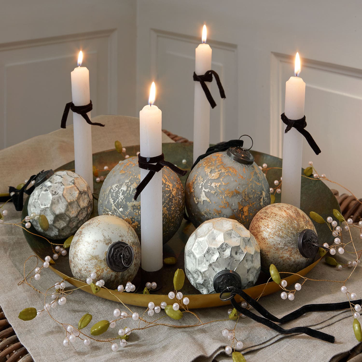Bandeja dorada decorativa con velas blancas y bolas metálicas vintage sobre mantel de lino